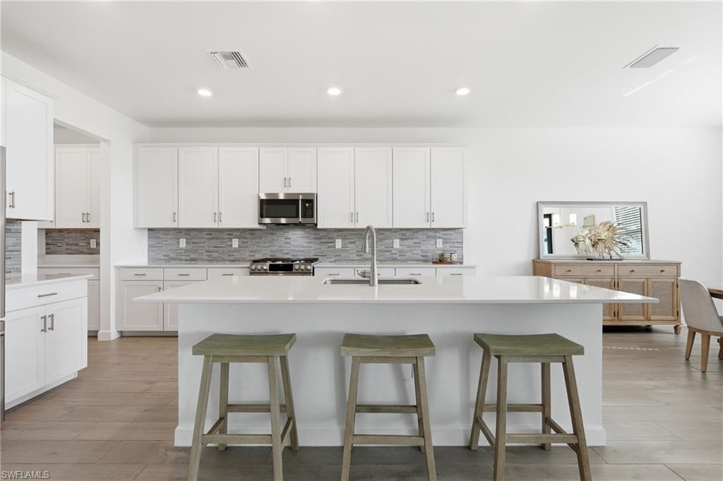 Modern white kitchen with a large island, three green stools, and gray tile backsplash.