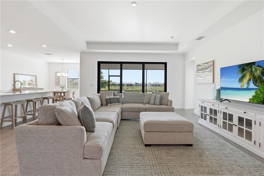 Furnished living room with a gray sectional, ottoman, and large black-framed windows.