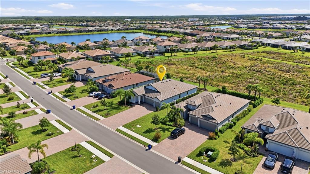Aerial view of the marked home beside undeveloped green land, with a neighborhood lake in the distance.