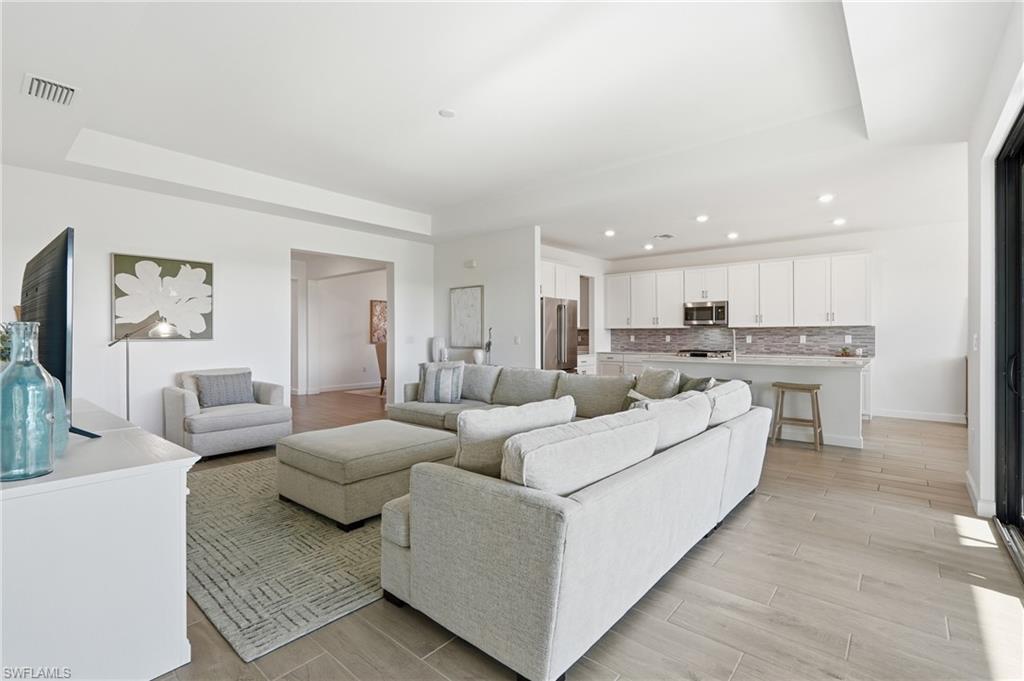 Open-plan living room and kitchen with a large sectional, white cabinets, and light wood-look flooring.