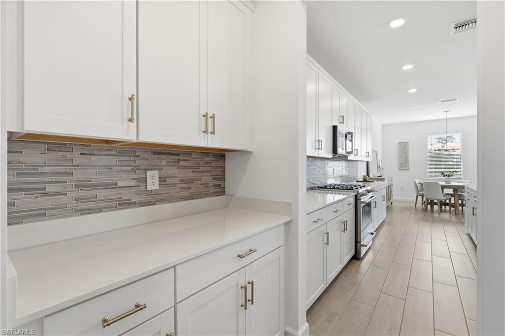 Kitchen with white cabinetry, gray tile backsplash, stainless appliances, and a dining area beyond.