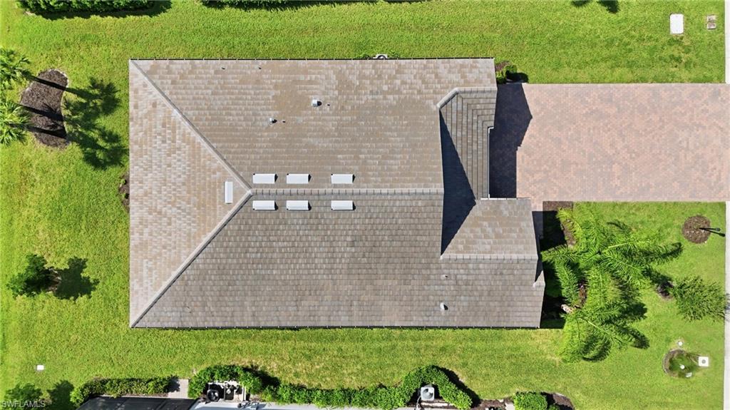 Aerial view of a gray-shingled home roof with skylights, driveway, lawn, and palm trees.