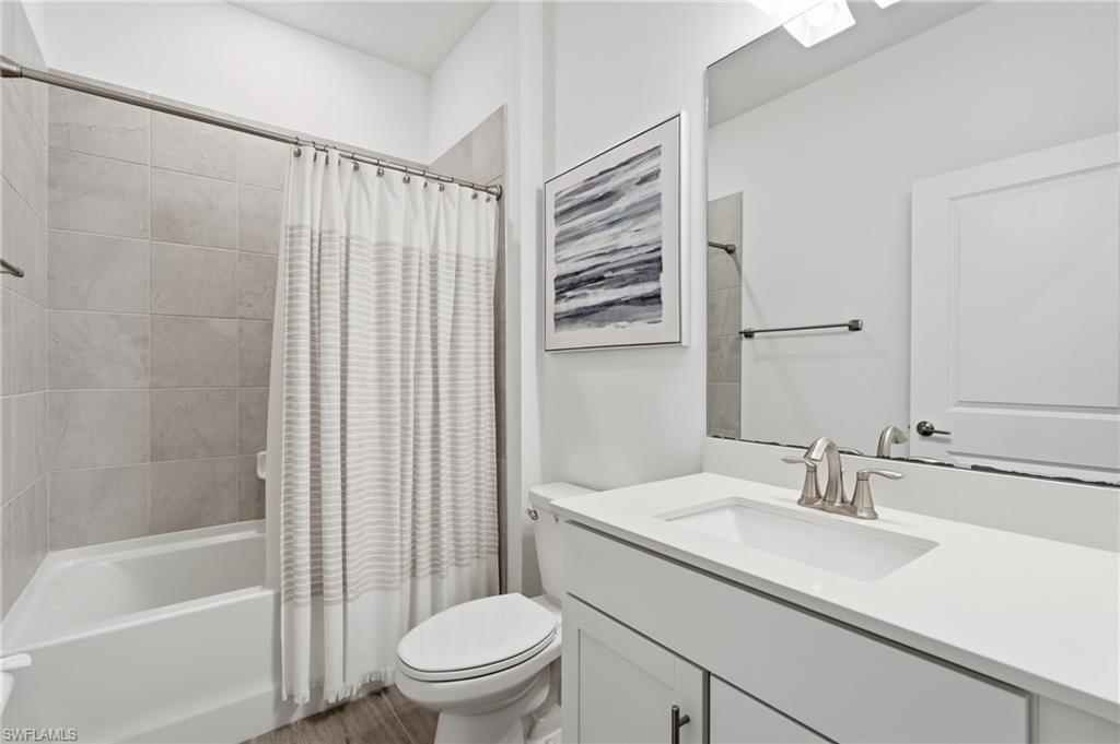 Bathroom with a white vanity and sink beside a tiled tub and striped shower curtain.