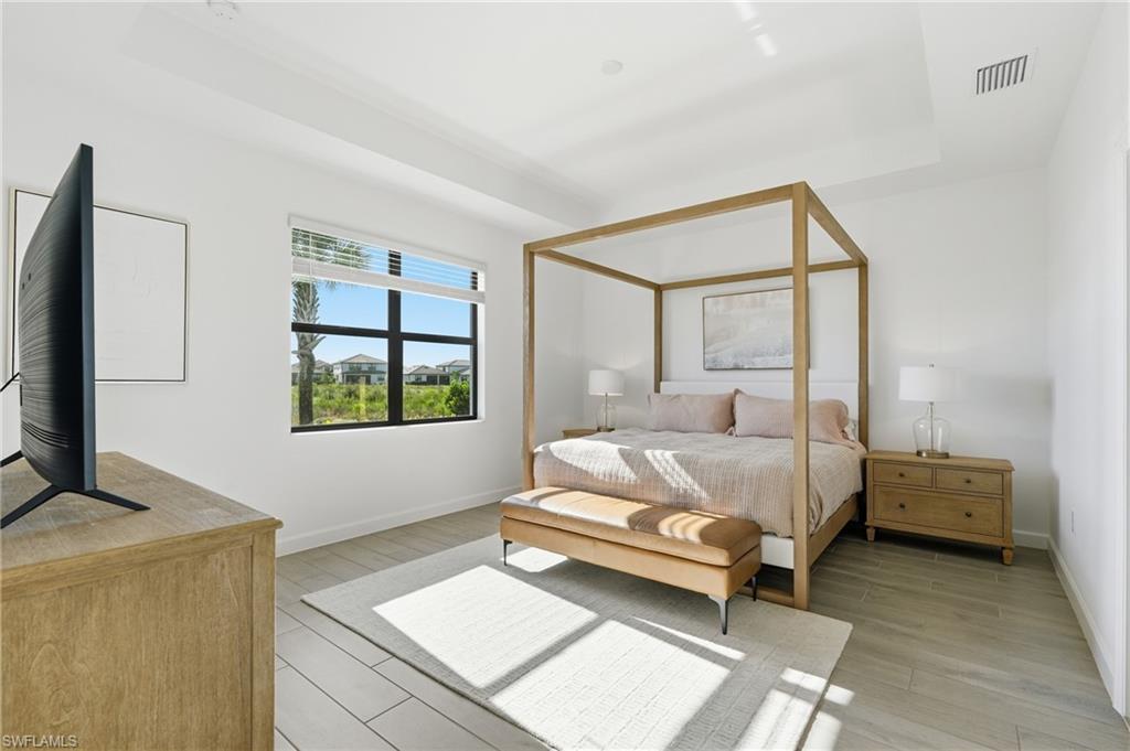 Bright bedroom with a canopy bed, wood furnishings, and a large window overlooking neighboring homes.