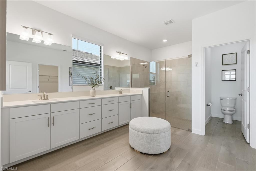 Bright bathroom with a long double vanity, glass-enclosed shower, and separate toilet room.
