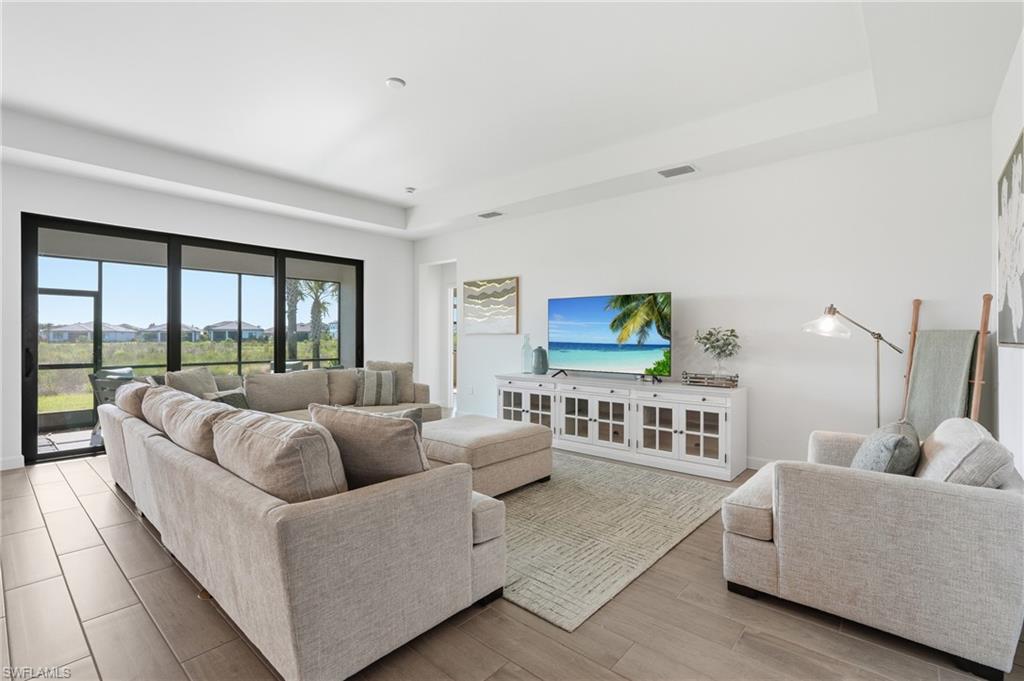 Furnished living room with a neutral sectional, large sliding glass doors, and white media console.