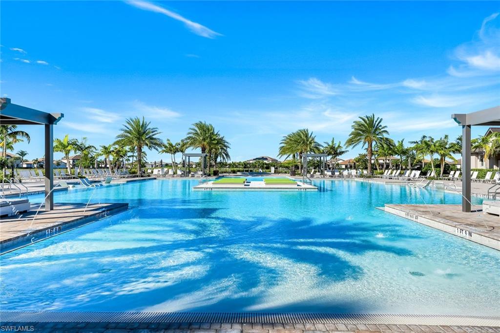 Outdoor community pool with palm trees and lounge chairs along the water.