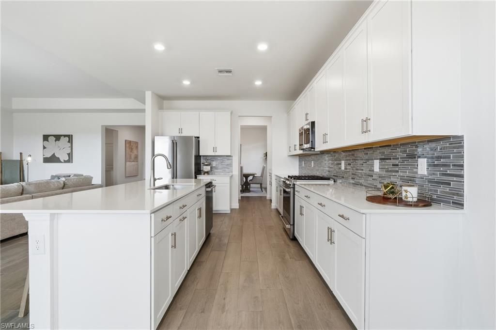 Bright kitchen with white cabinets, a large island, gray tile backsplash, and stainless steel appliances.