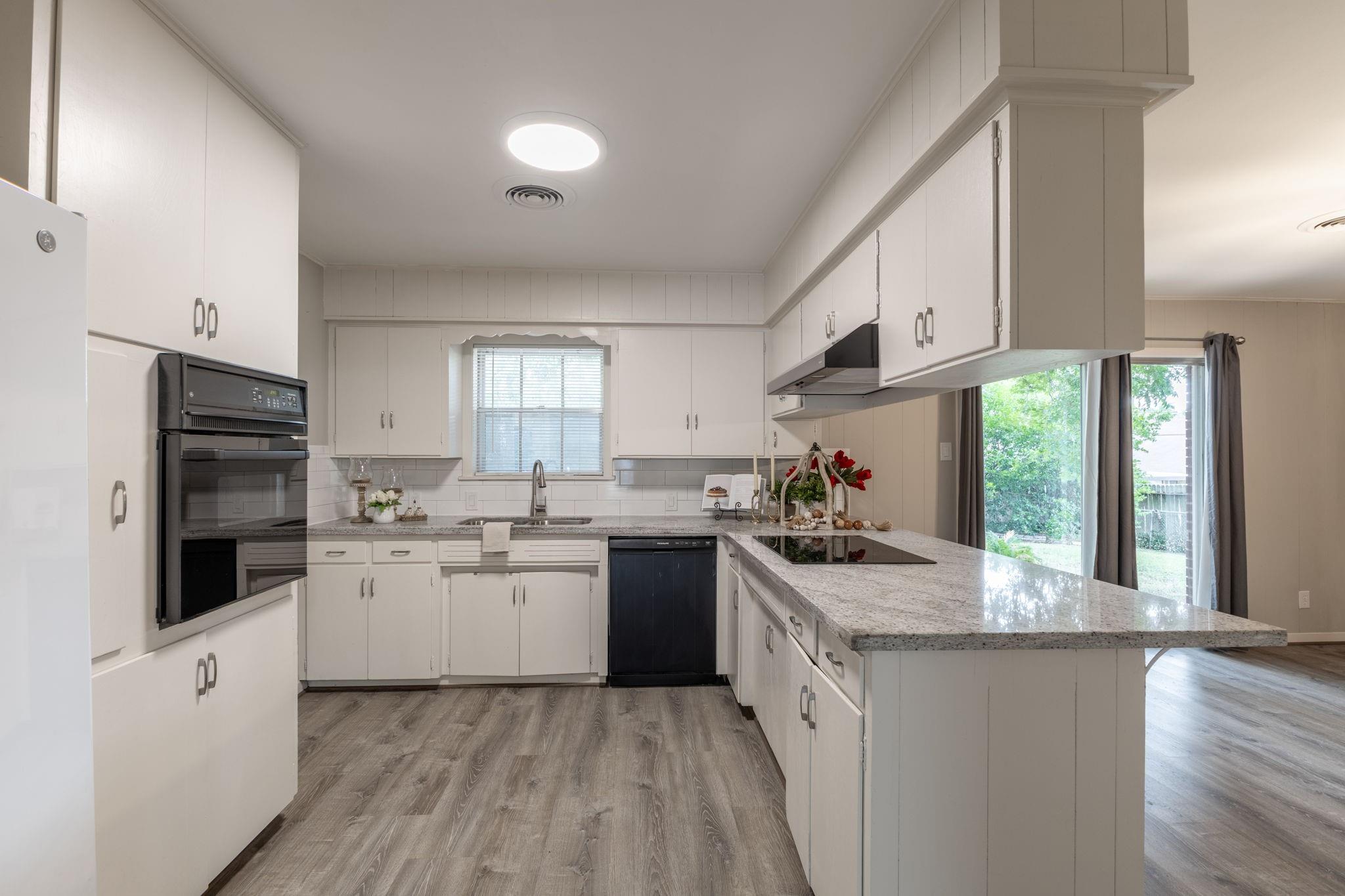 Kitchen with white cabinets, granite peninsula and cooktop, built-in oven, and sliding glass door.