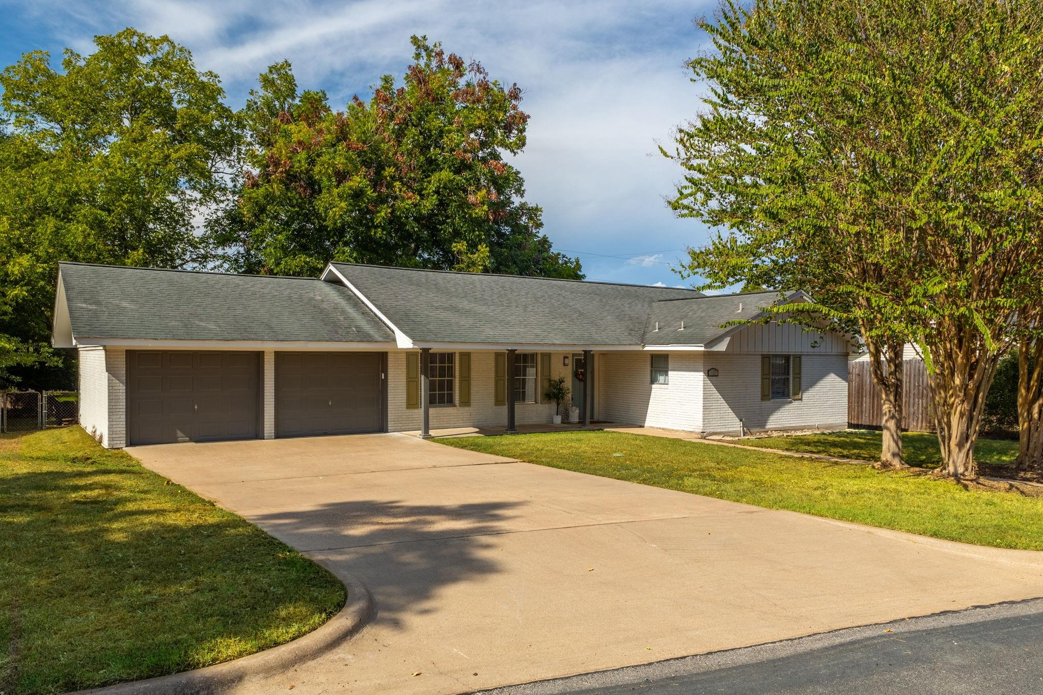 Single-story white-brick home with a two-car garage, covered porch, and broad driveway.
