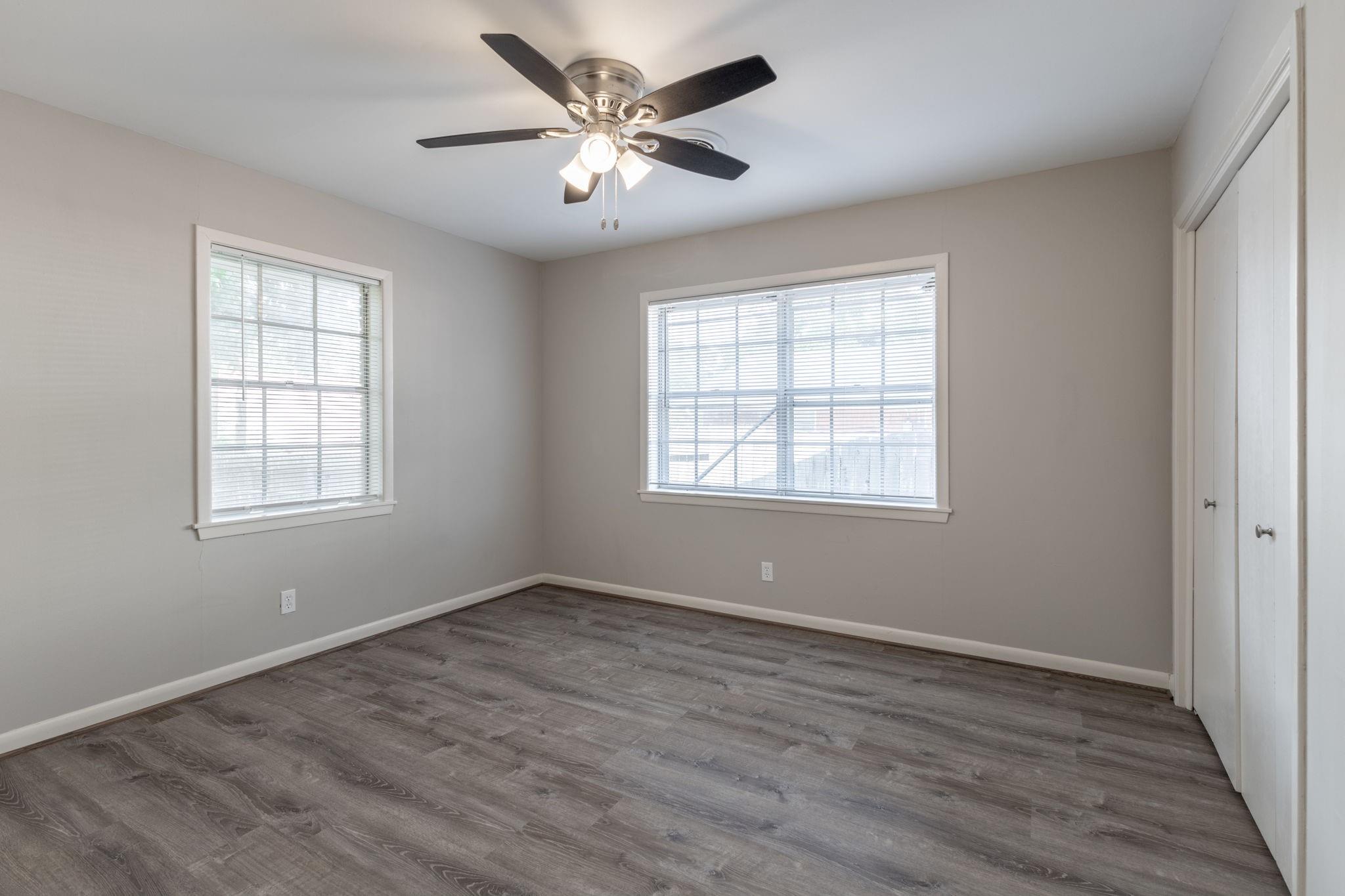 Vacant bedroom with gray wood-look flooring, two windows, and a ceiling fan.