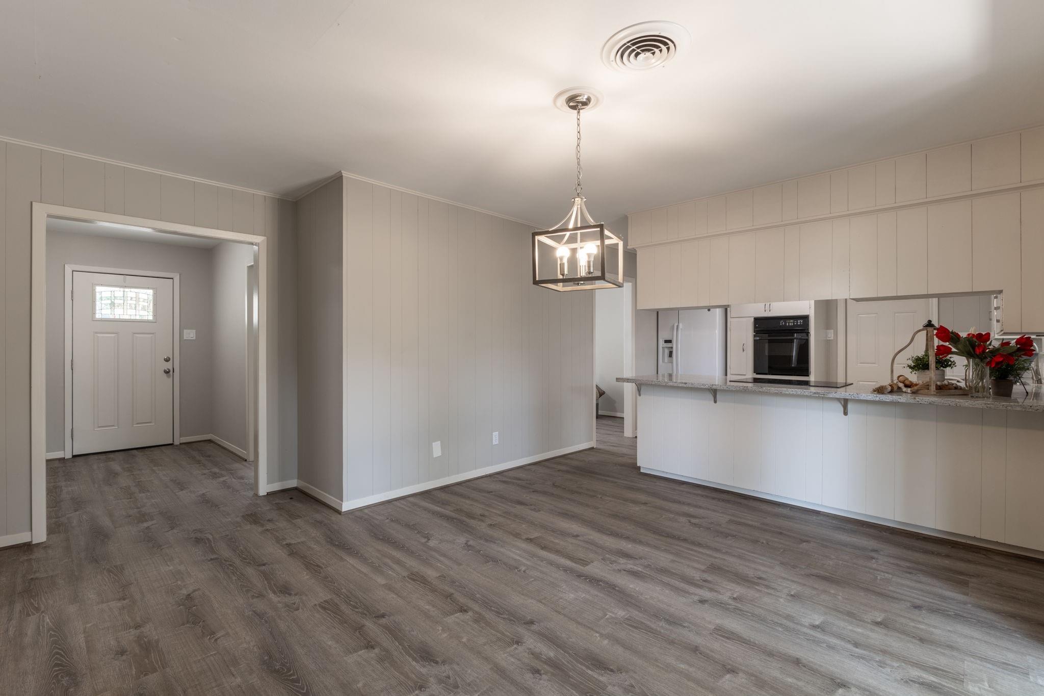 Open dining area and kitchen with gray flooring, white cabinetry, and a long breakfast bar.