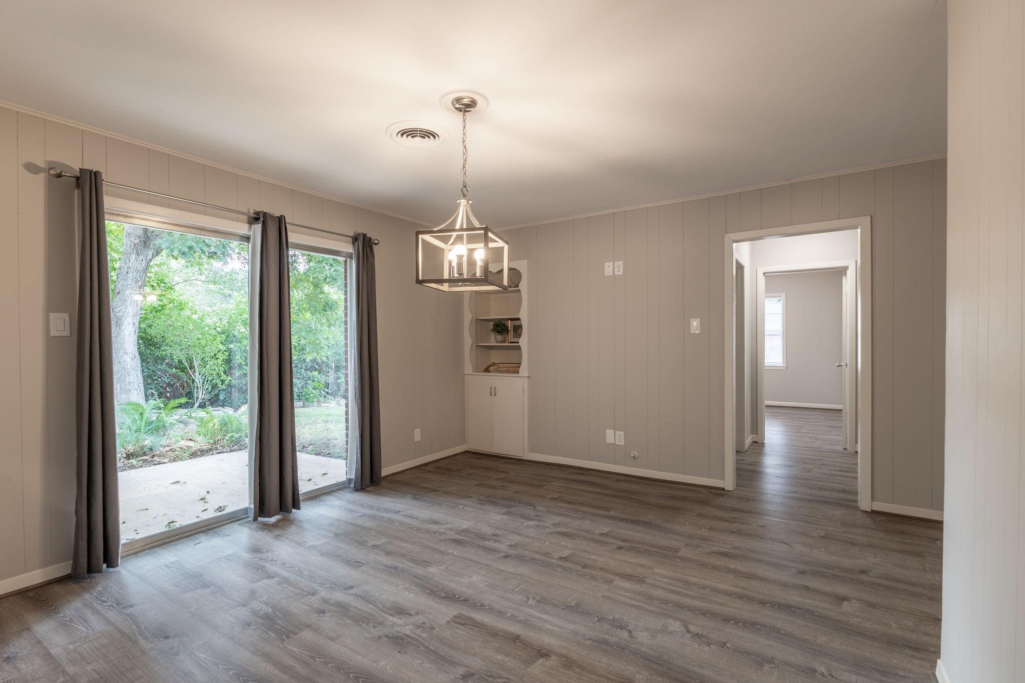 Vacant dining room with a chandelier, built-in corner shelves, and glass doors opening to a garden.