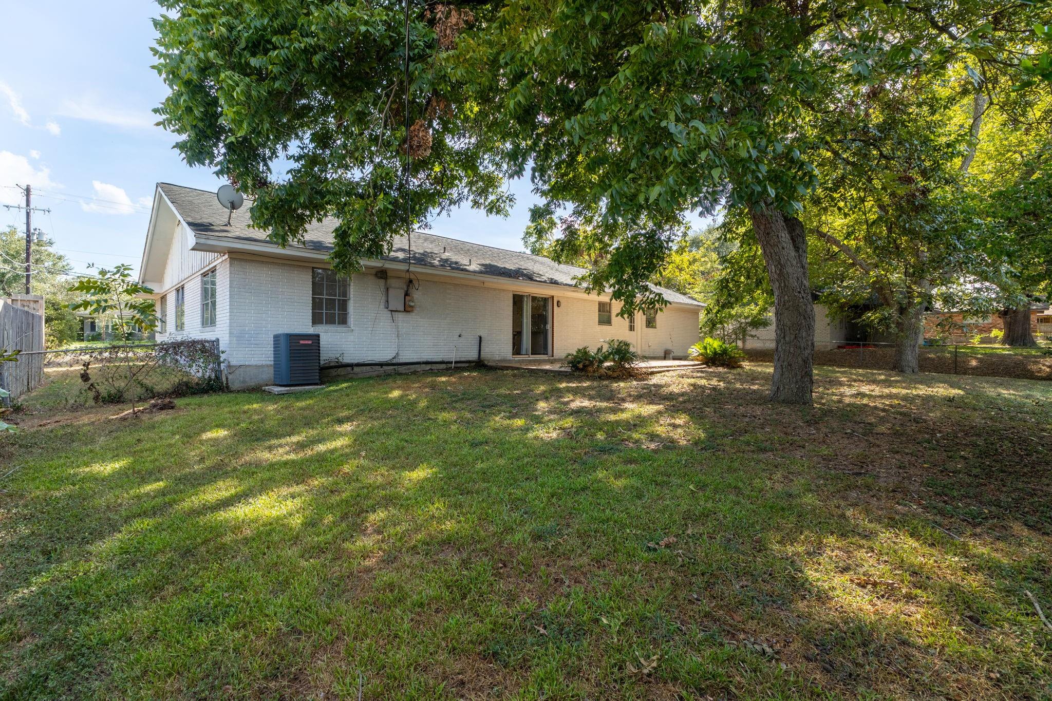 White brick house viewed from the backyard, with mature shade trees and a sliding glass door.