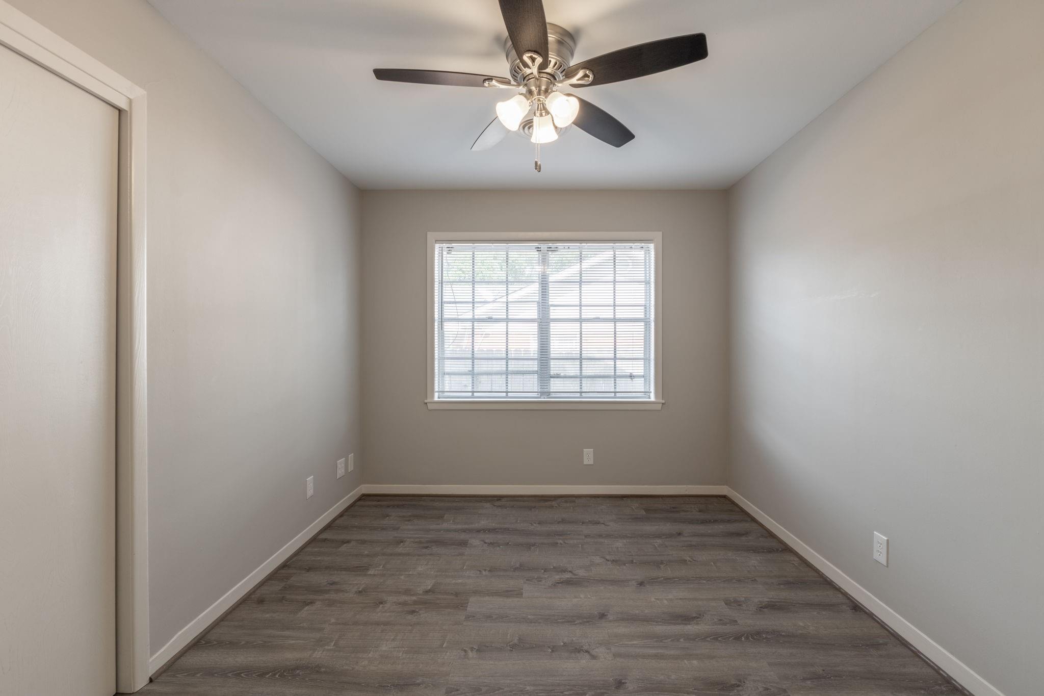 Vacant room with gray wood-look flooring, a window with blinds, and a ceiling fan with lights.