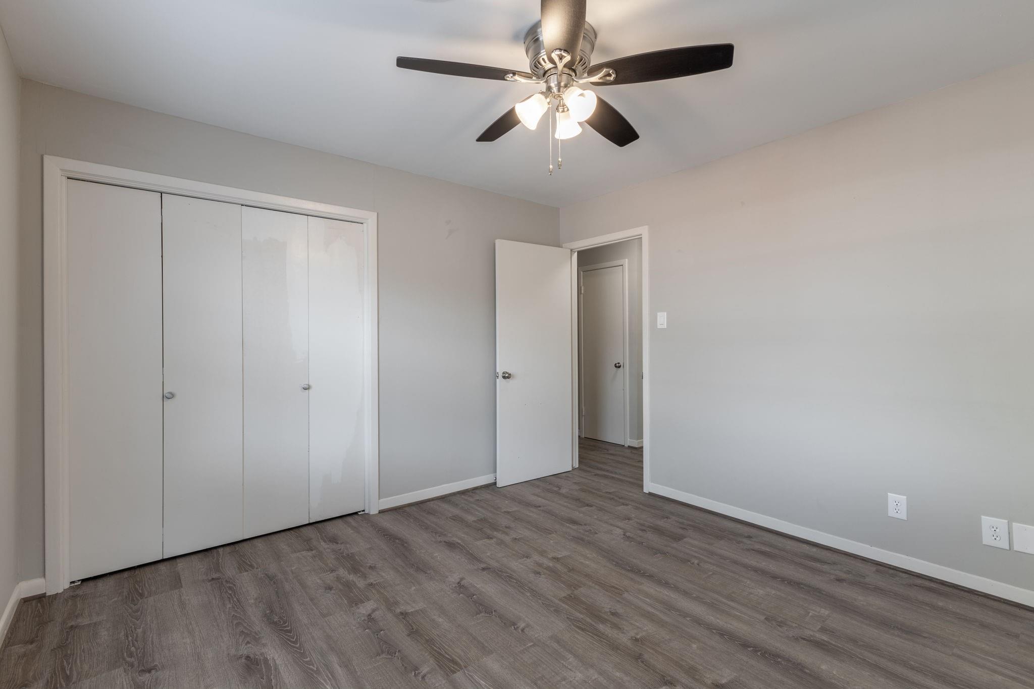 Empty bedroom with gray wood-look flooring, a white closet, and a ceiling fan.
