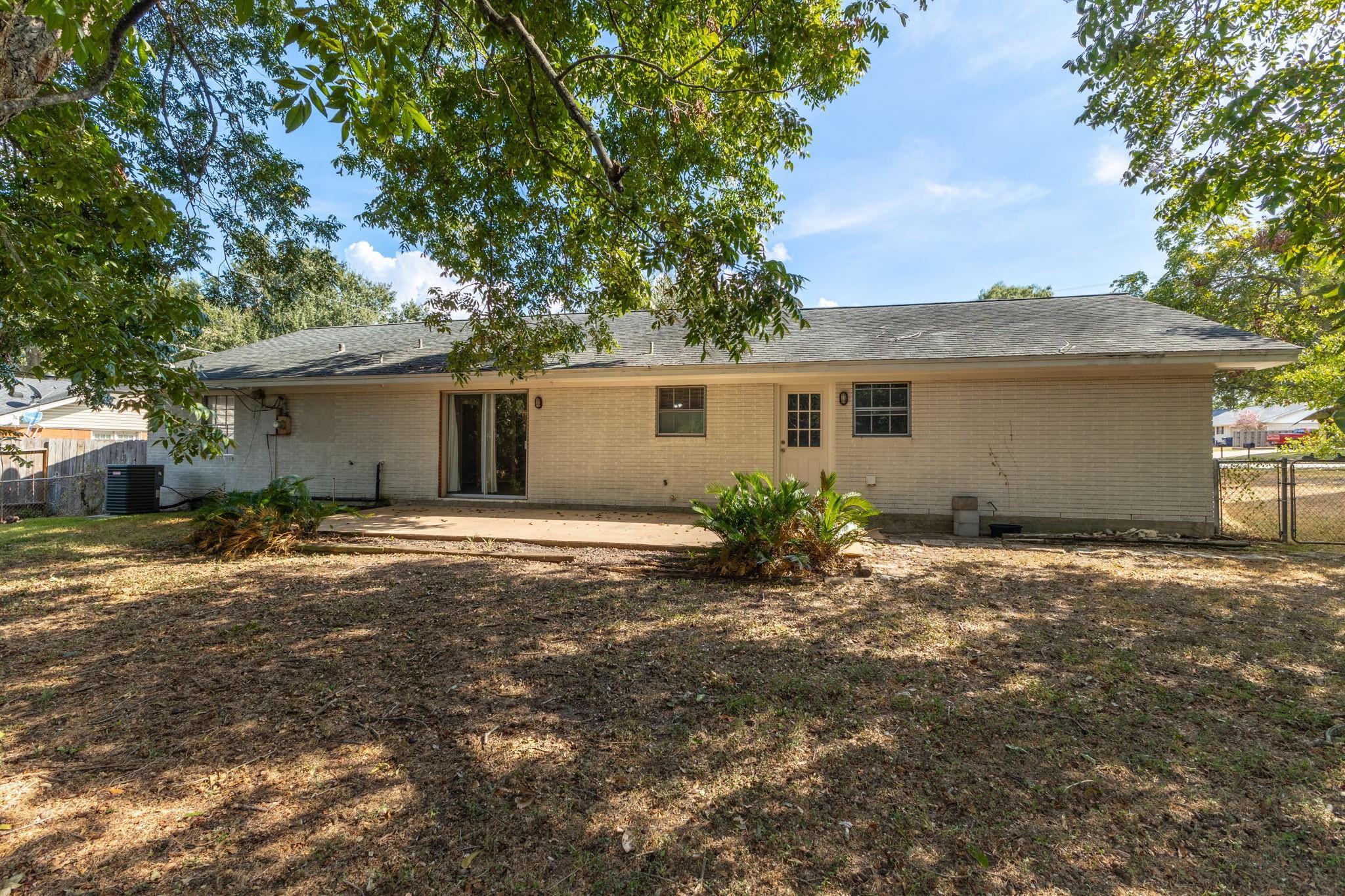 Rear of a single-story brick house with a sliding glass door and a large shaded yard.