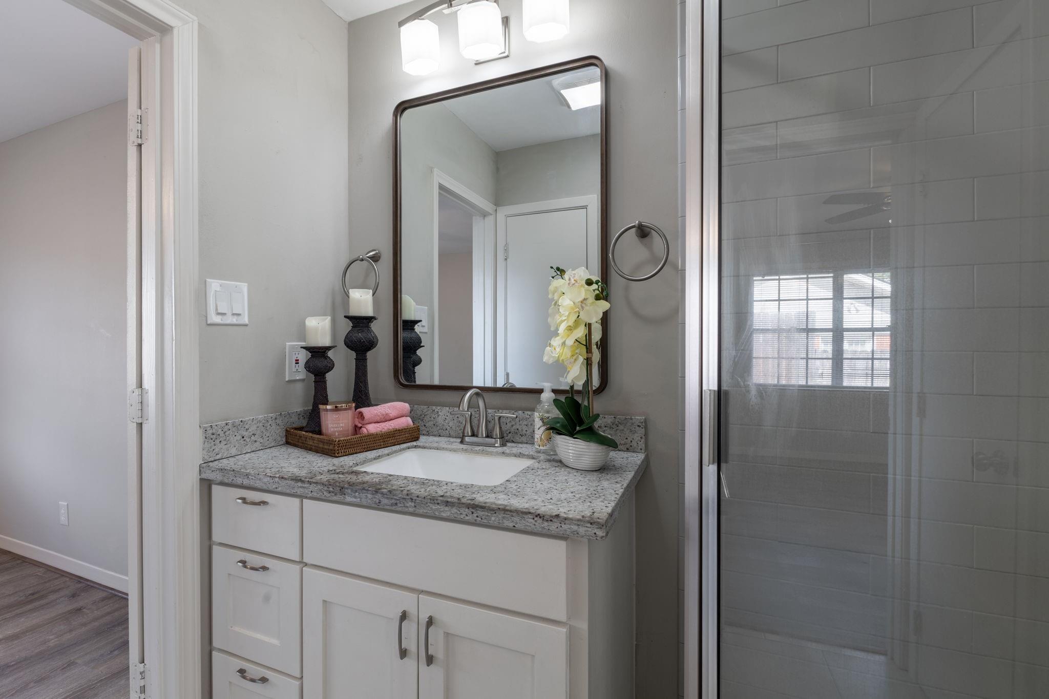 Bathroom vanity with speckled granite counter, framed mirror, and glass-enclosed tiled shower.