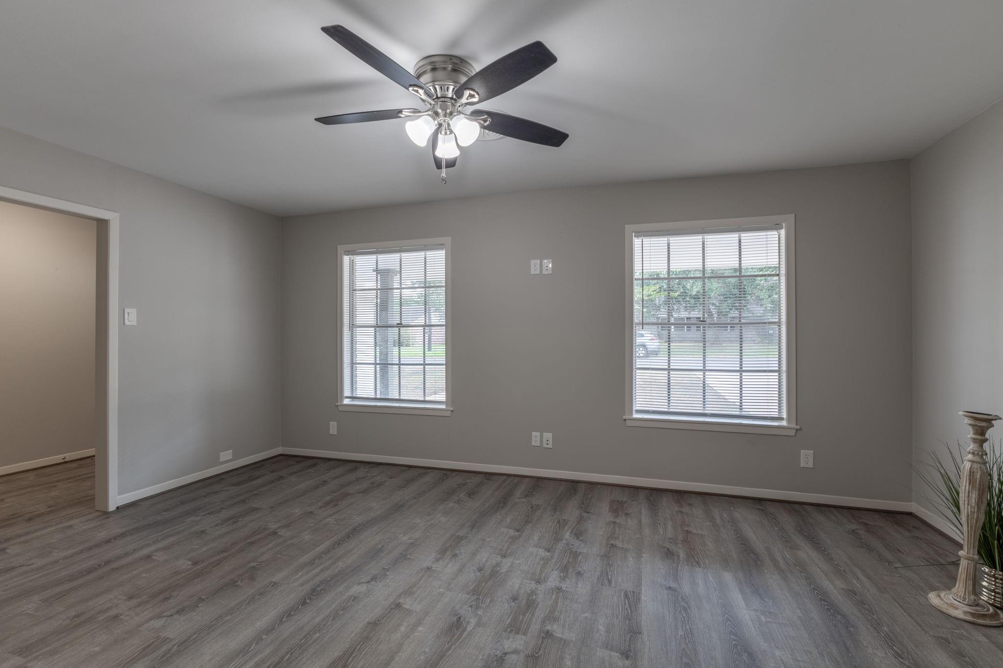 Unfurnished room with gray wood-look floors, two blinded windows, and a ceiling fan.