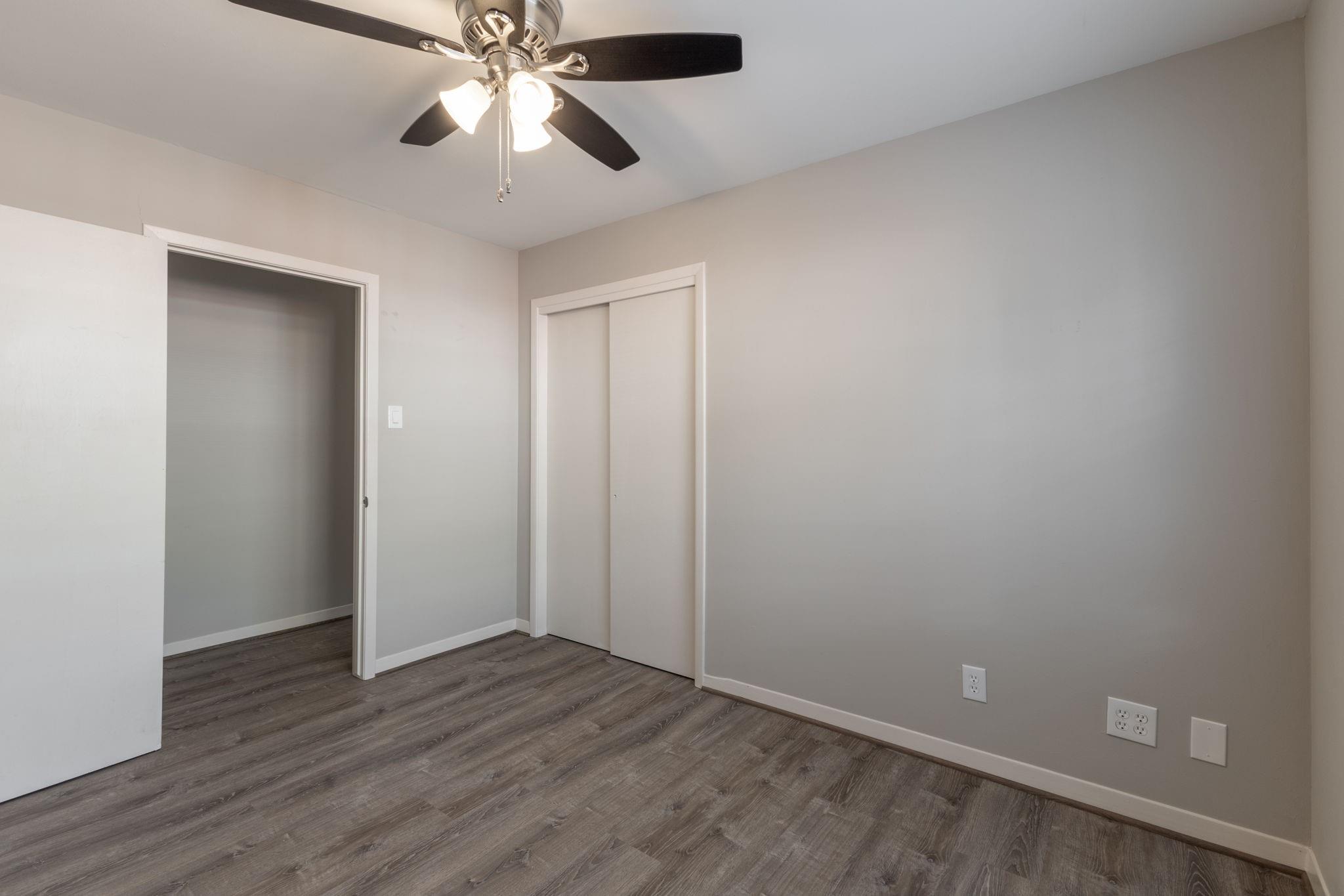 Empty bedroom with gray wood-look floors, ceiling fan, and sliding-door closet.