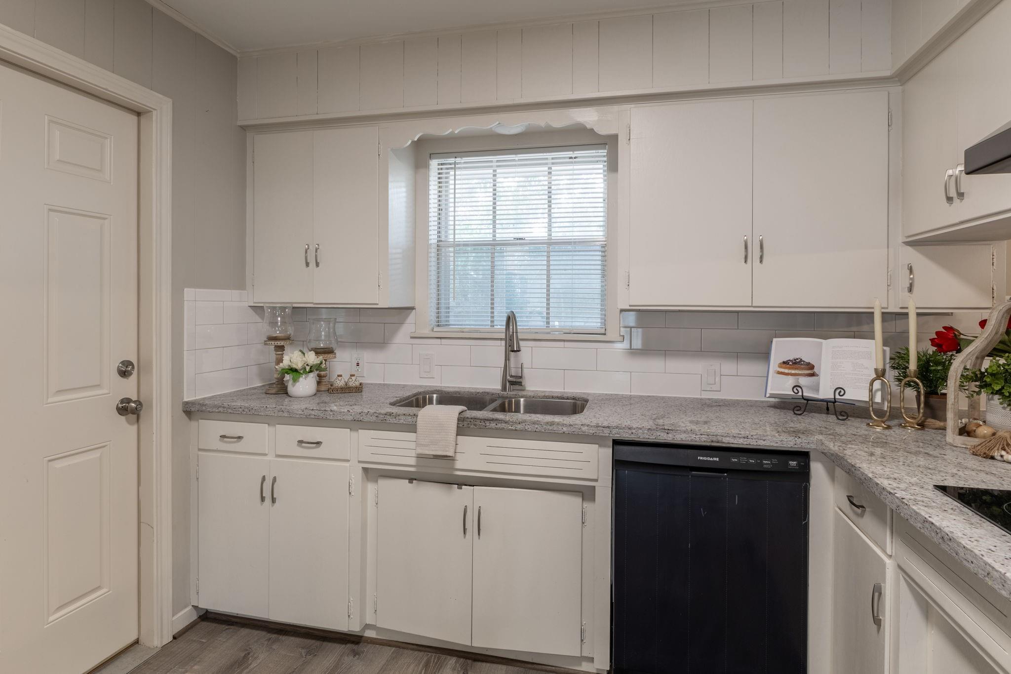 Kitchen with white cabinets, gray countertops, and a double sink beneath a window.
