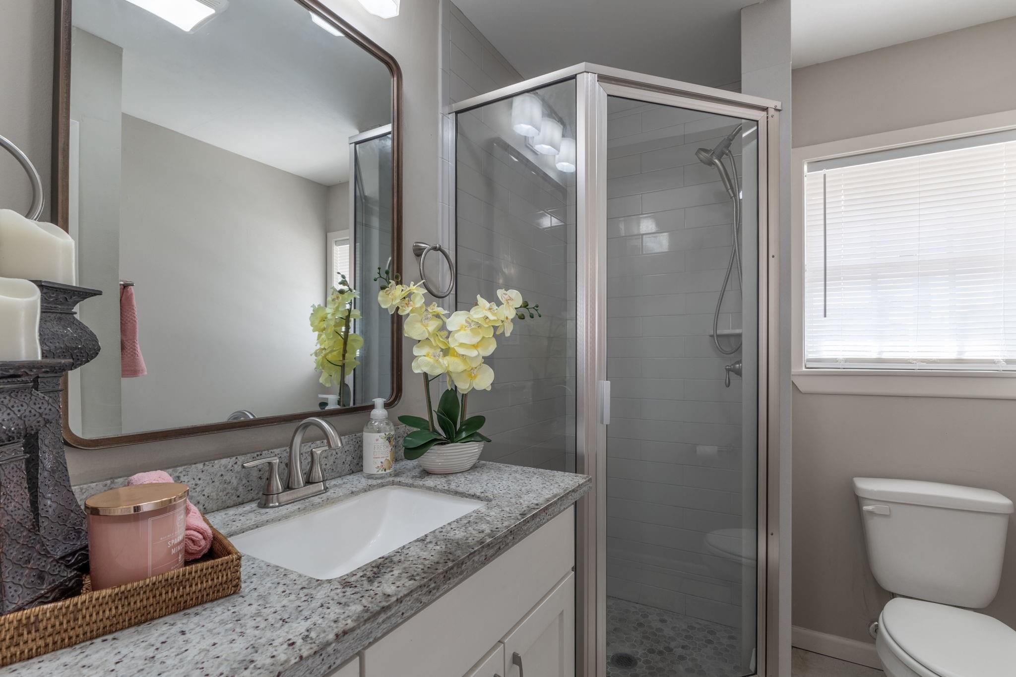 Bathroom with granite vanity and glass-enclosed tiled shower beside a window.