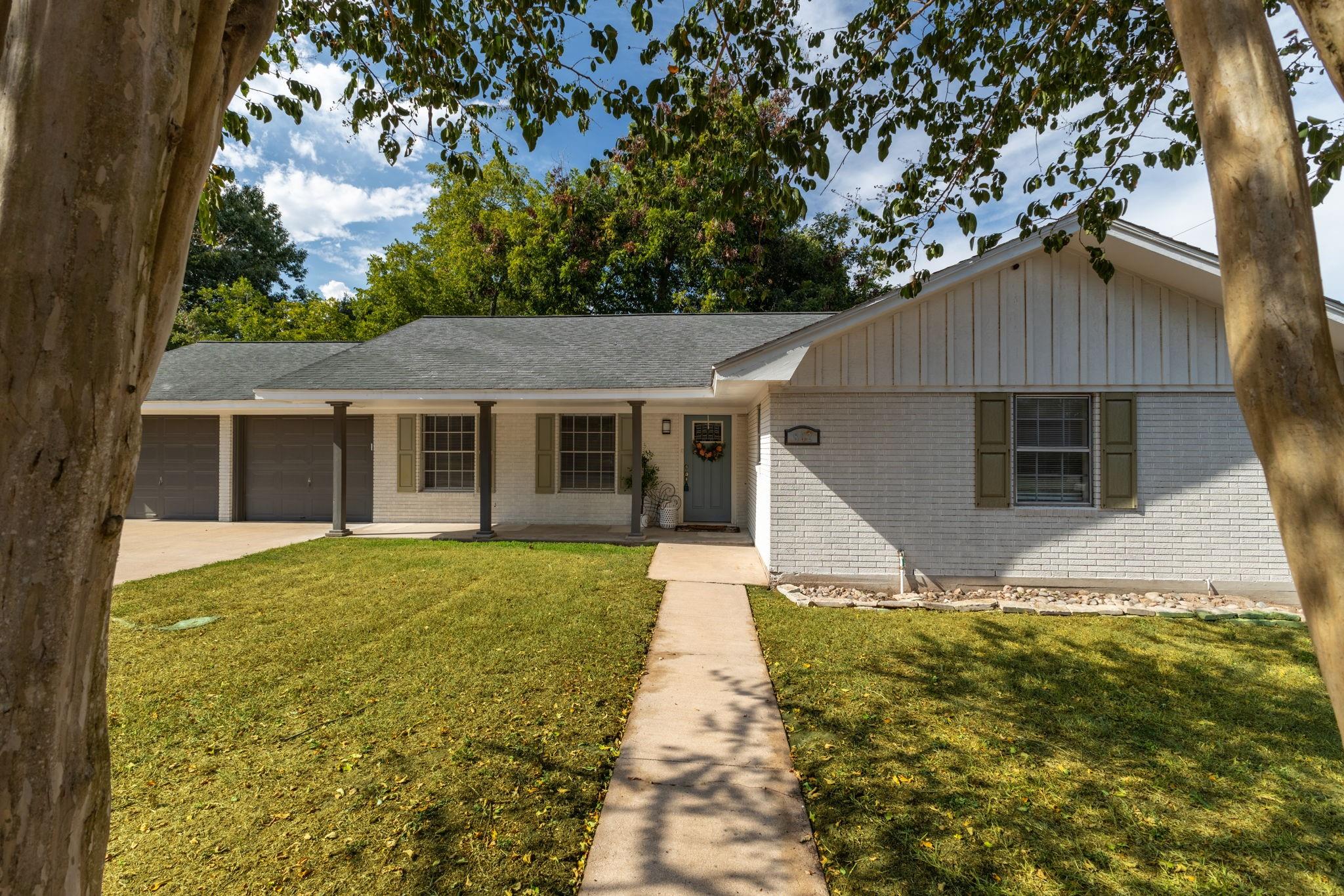 Single-story brick house with a covered porch, two-car garage, and walkway across the front lawn.