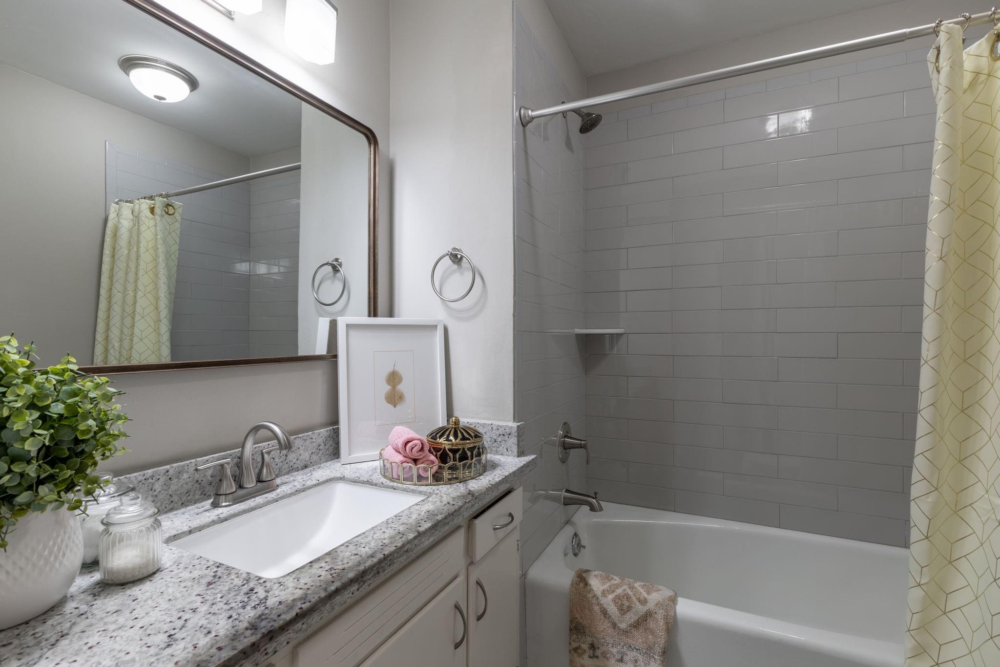 Bathroom with a granite vanity, large mirror, and gray subway-tile bathtub surround.