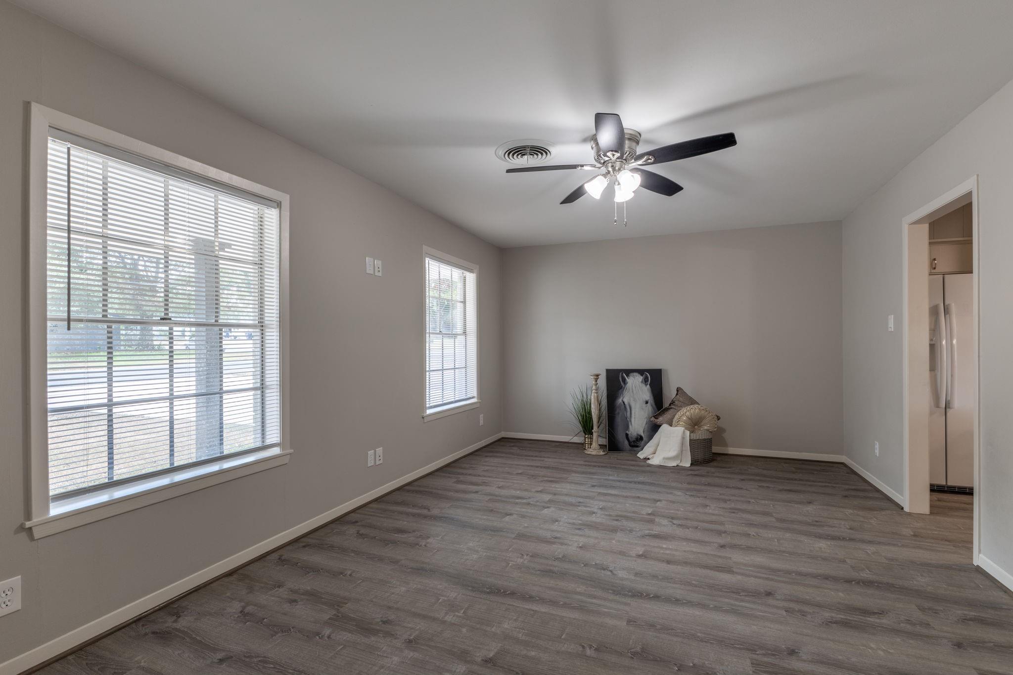 Mostly empty room with gray plank flooring, two blinded windows, and a ceiling fan.