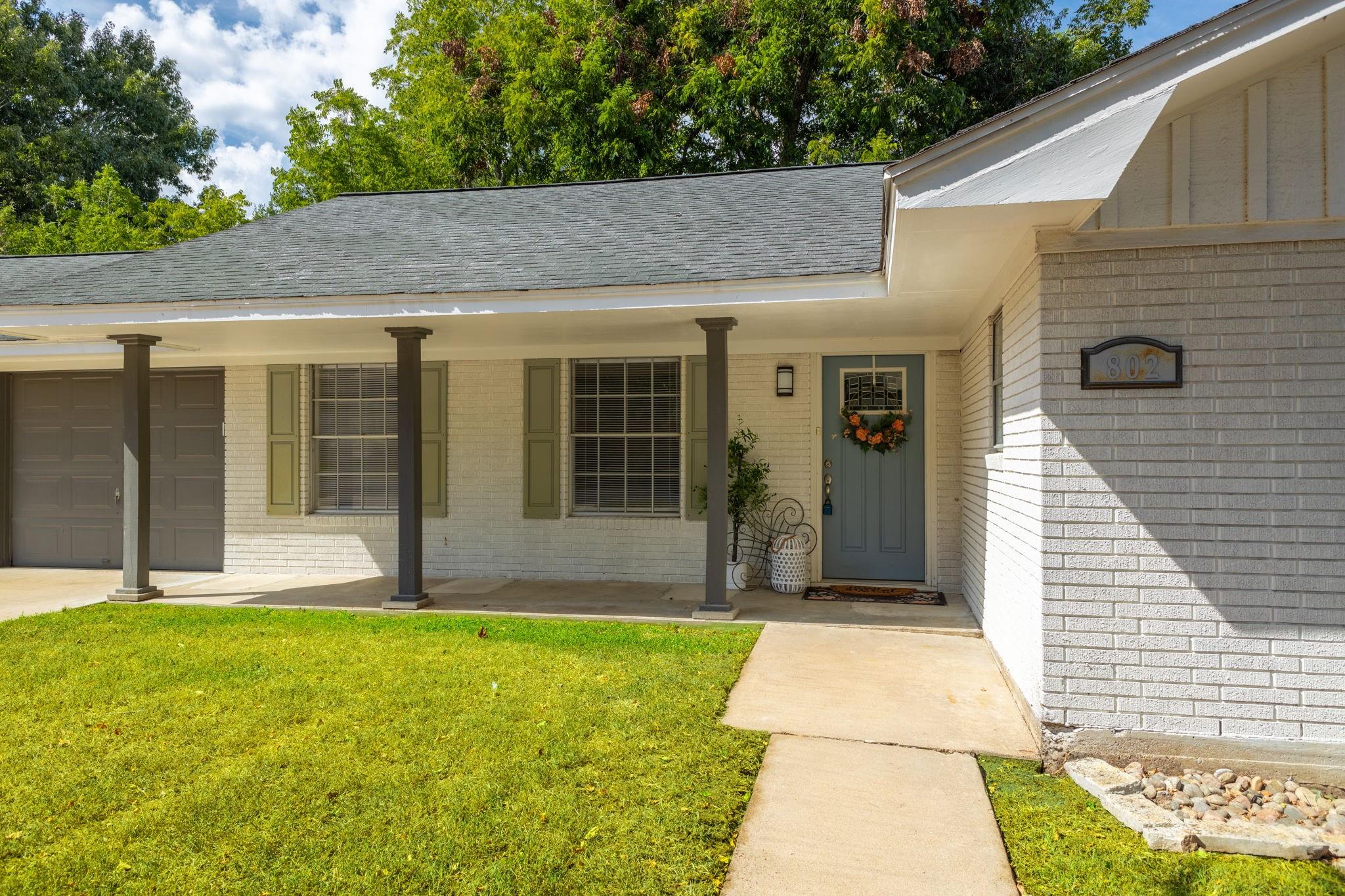 Light-brick home with a covered porch, attached garage, and blue-gray front door.