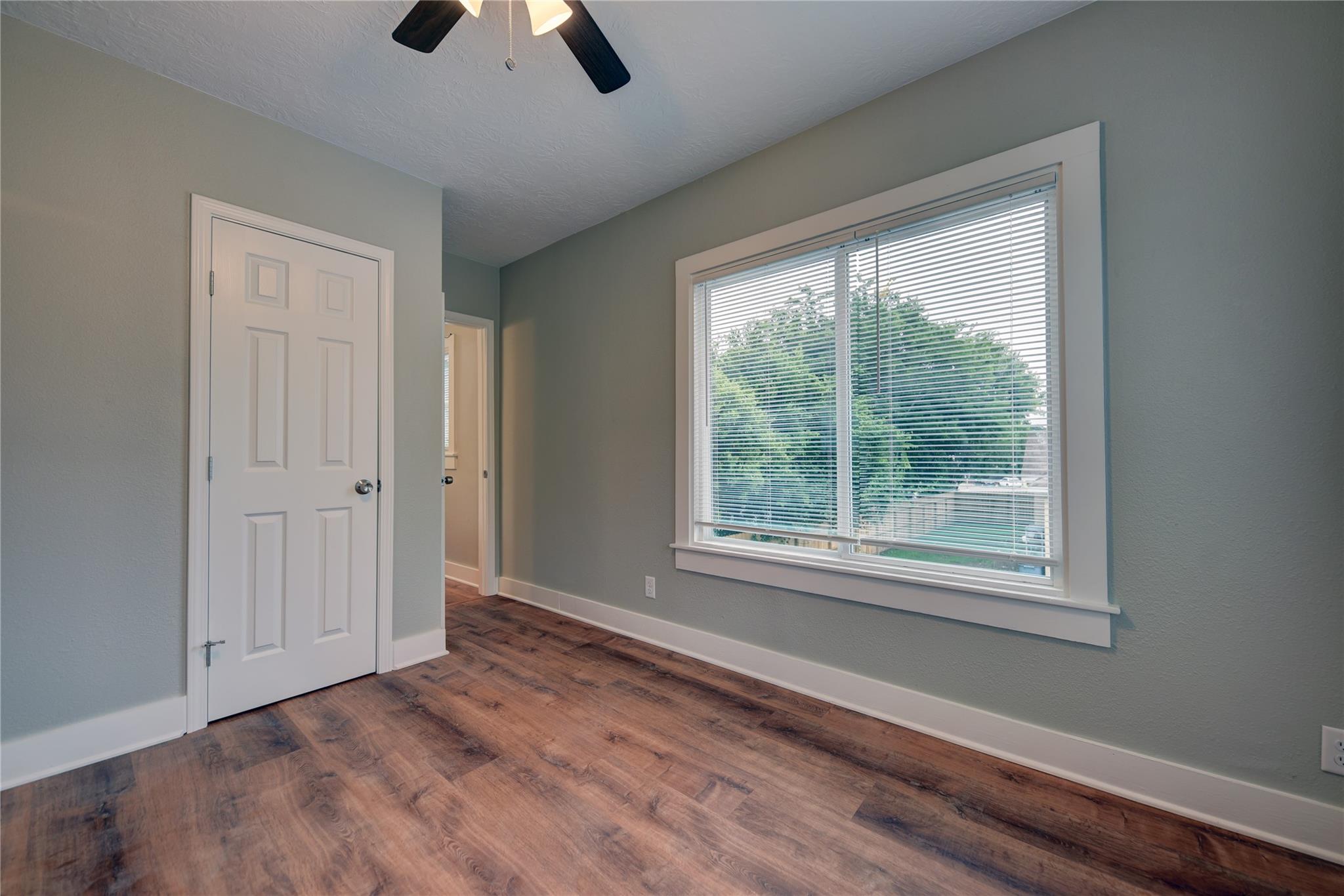 Empty room with dark wood-look flooring and a large window with blinds overlooking trees.