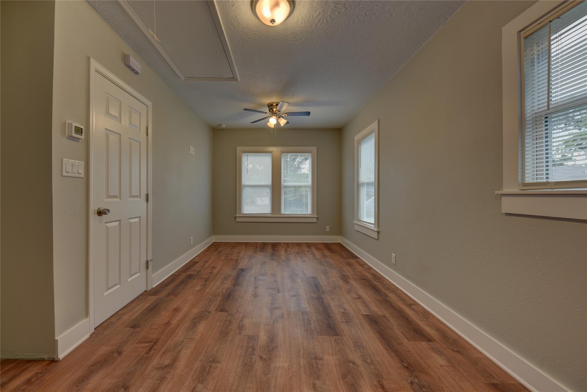 Empty room with wood-look flooring, multiple blinded windows, and a ceiling fan.