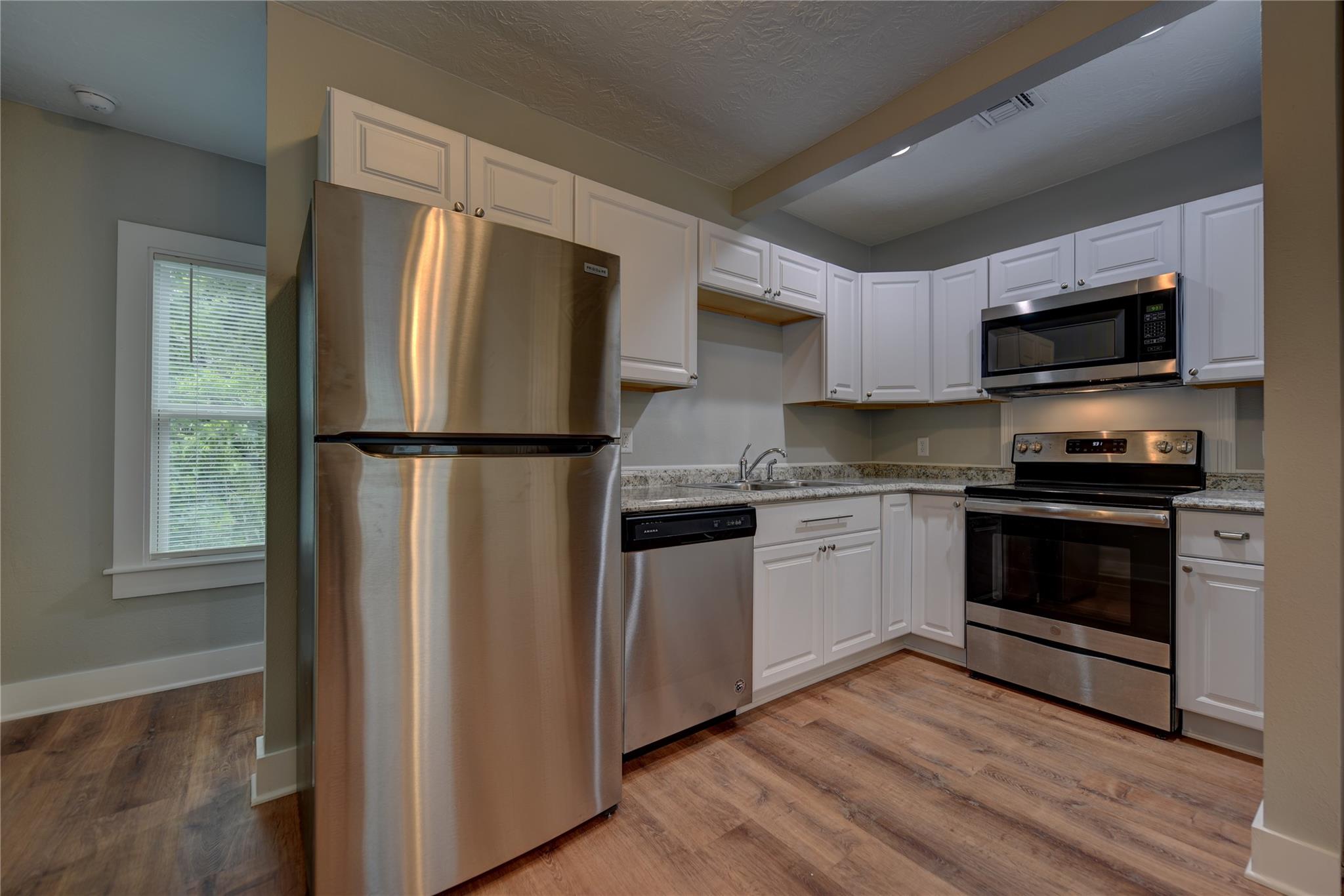 Kitchen with white cabinets, granite counters, stainless steel appliances, and wood-look flooring.