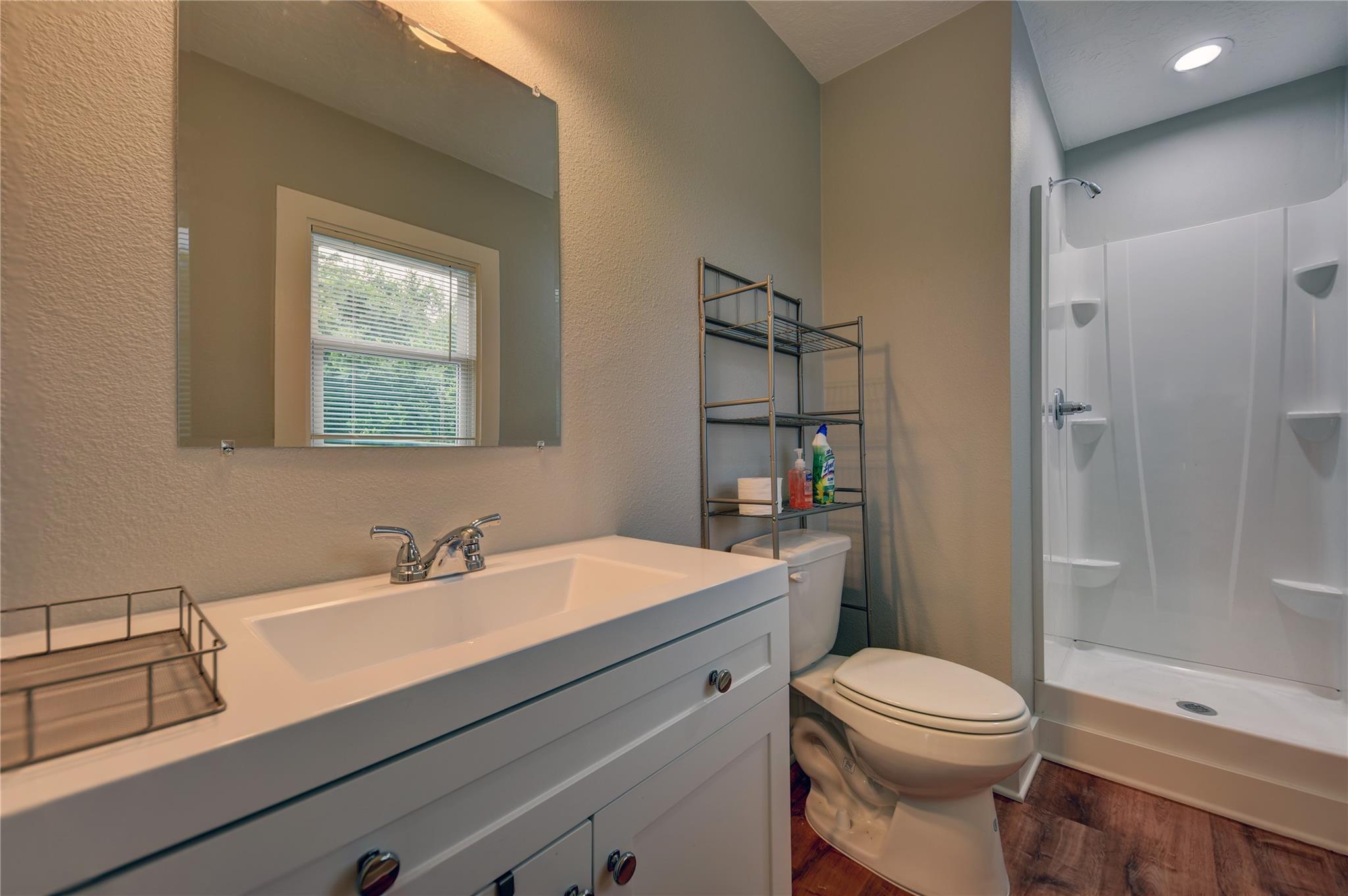 Bathroom with white vanity, toilet, and walk-in shower with built-in shelves.