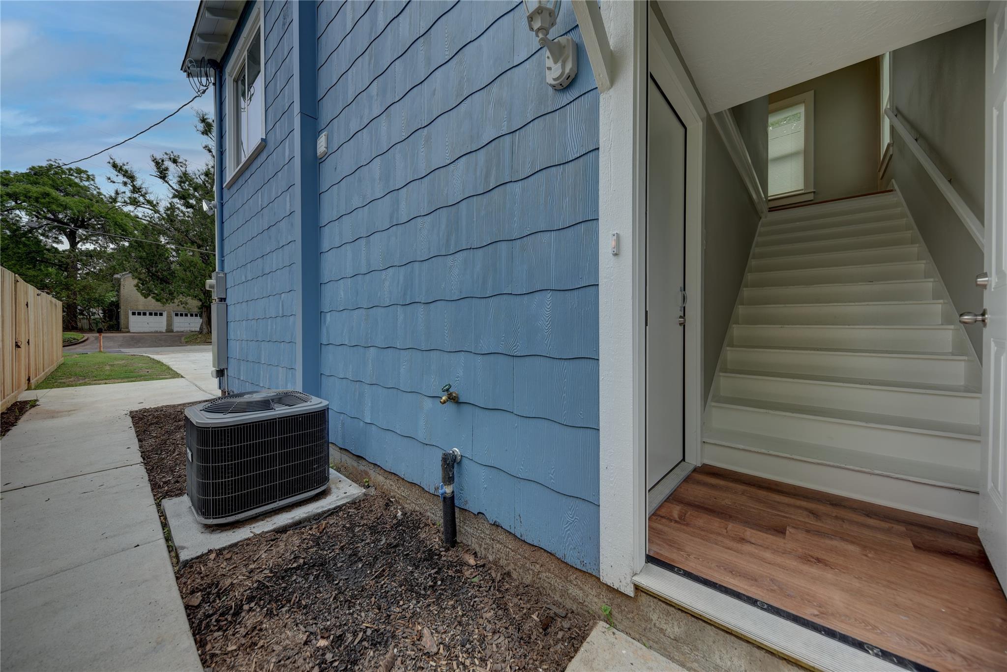 Blue-sided home entrance with an outdoor air-conditioning unit and staircase visible through the open door.