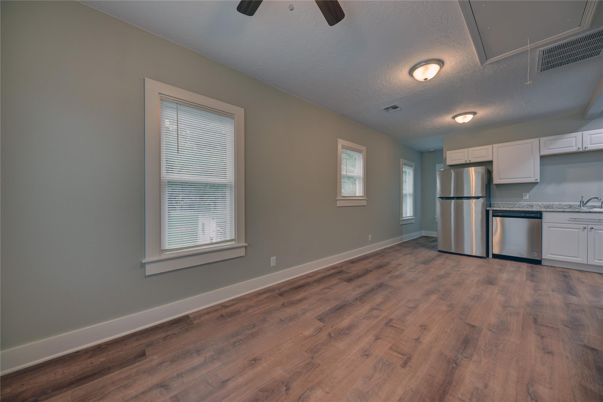 Empty kitchen with white cabinets, stainless steel appliances, and wood-look flooring.