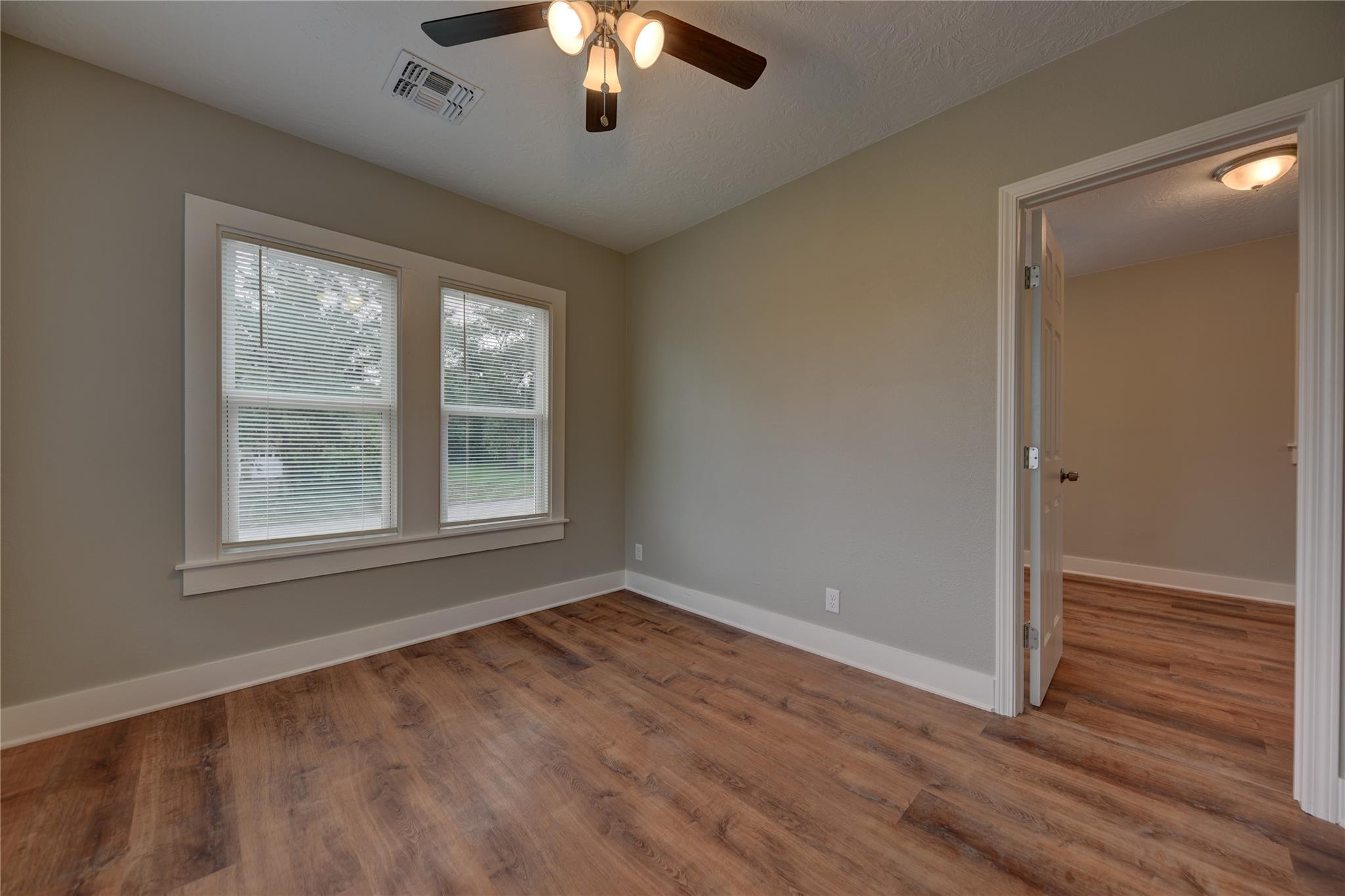 Empty room with wood-look flooring, two blind-covered windows, and a ceiling fan.