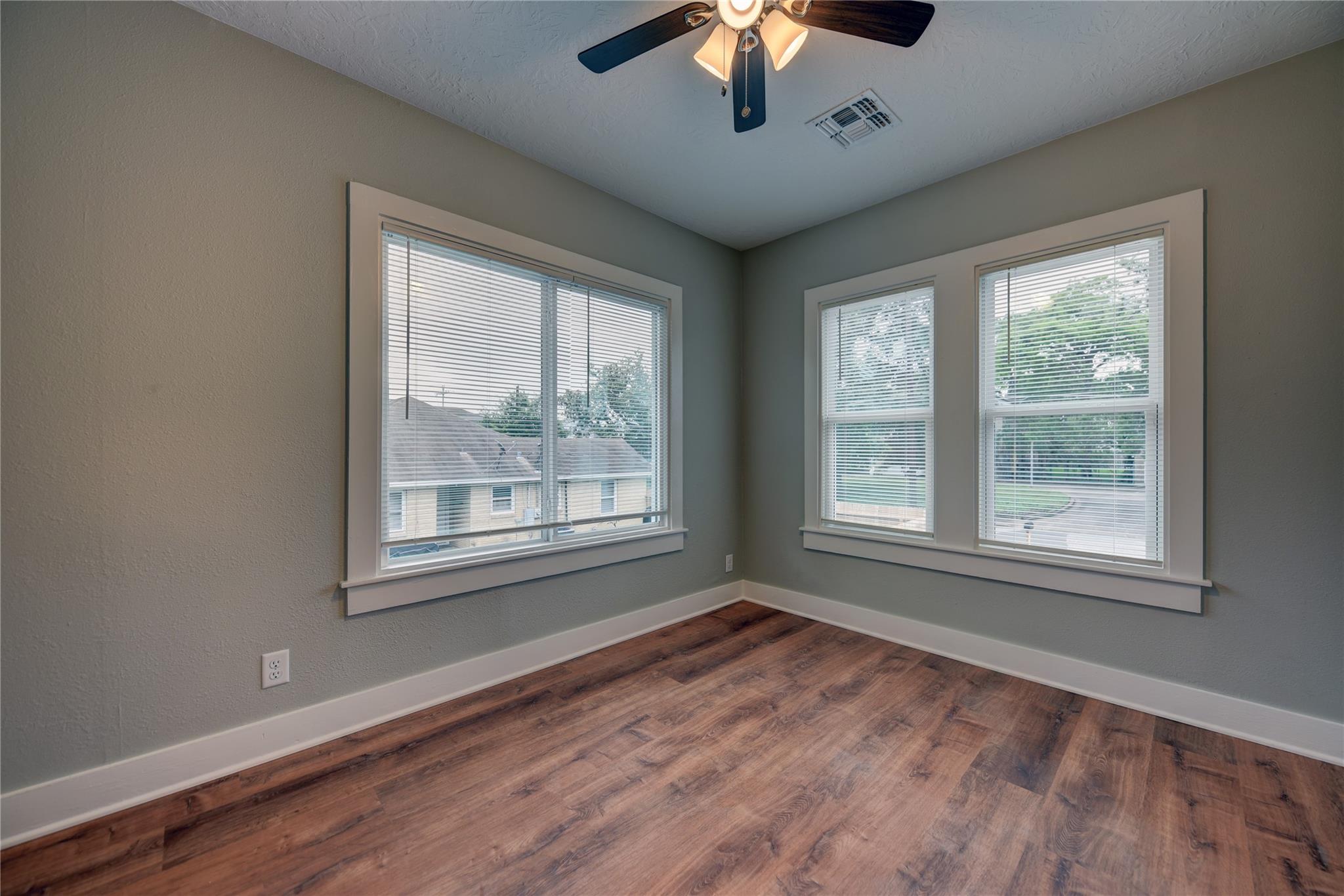 Empty room with wood-look flooring, gray walls, a ceiling fan, and three blind-covered windows.