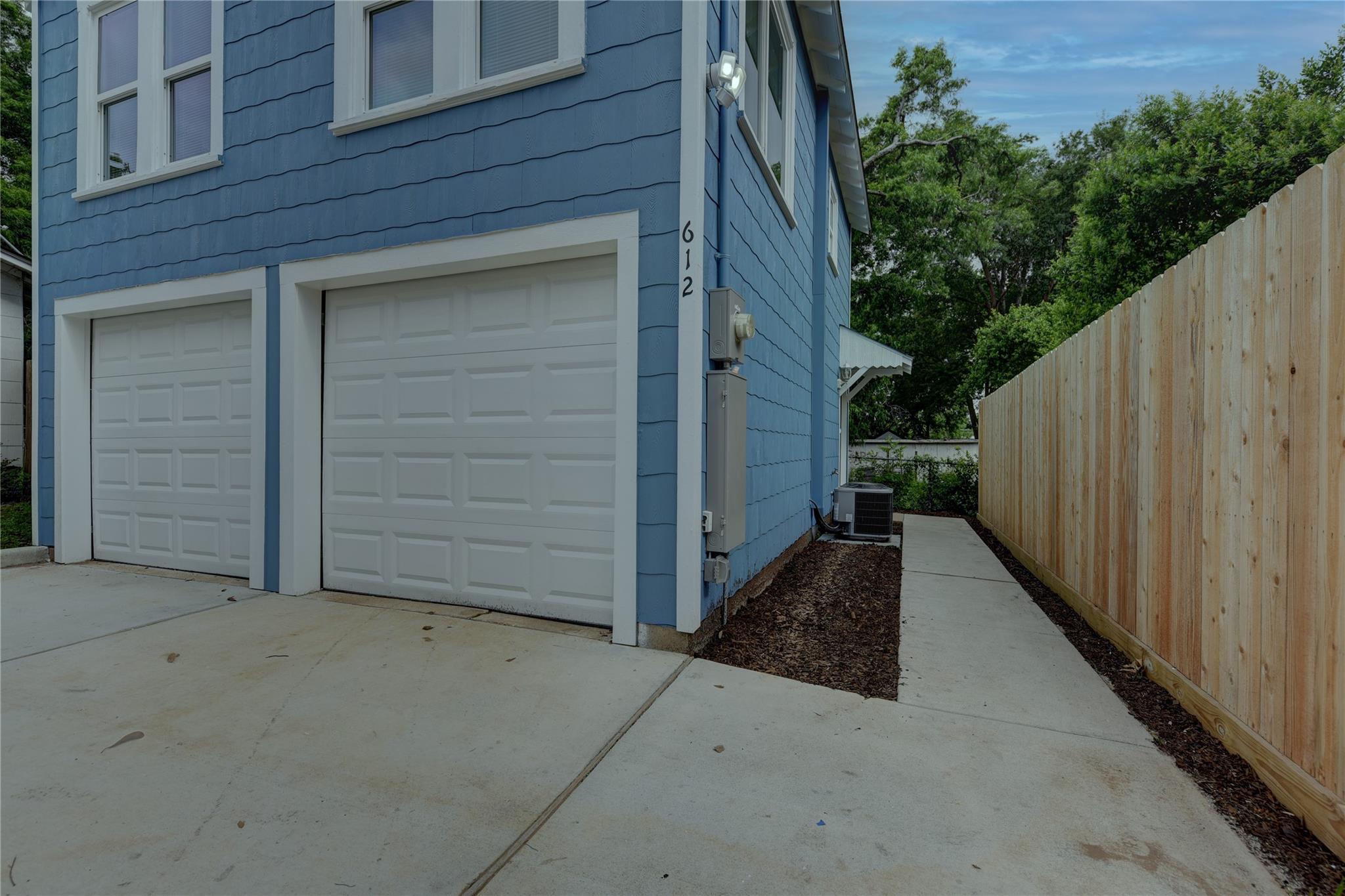 Blue-sided house with two white garage doors and a fenced concrete walkway.