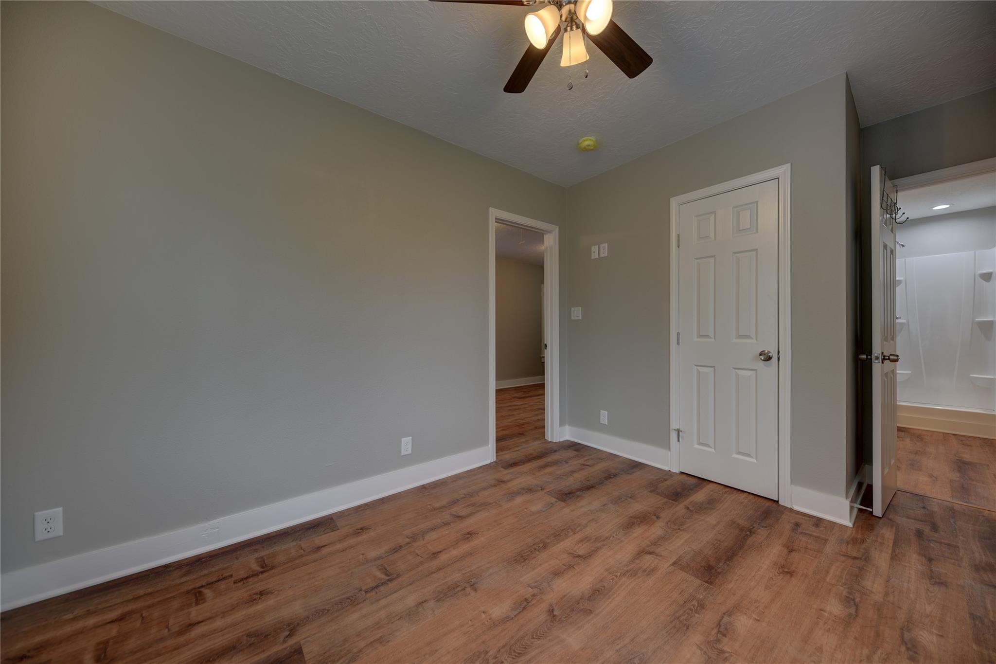 Empty bedroom with wood-look flooring, a ceiling fan, and an open doorway to a bathroom.