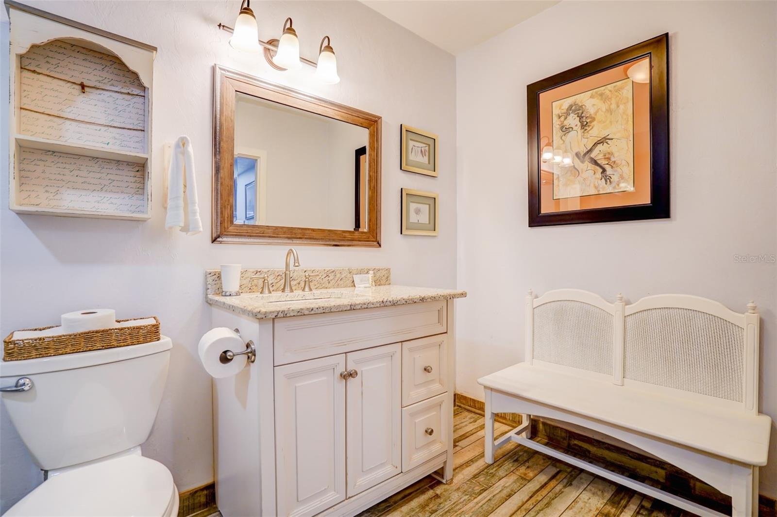 Bathroom with a white vanity, granite countertop, large mirror, and white bench.