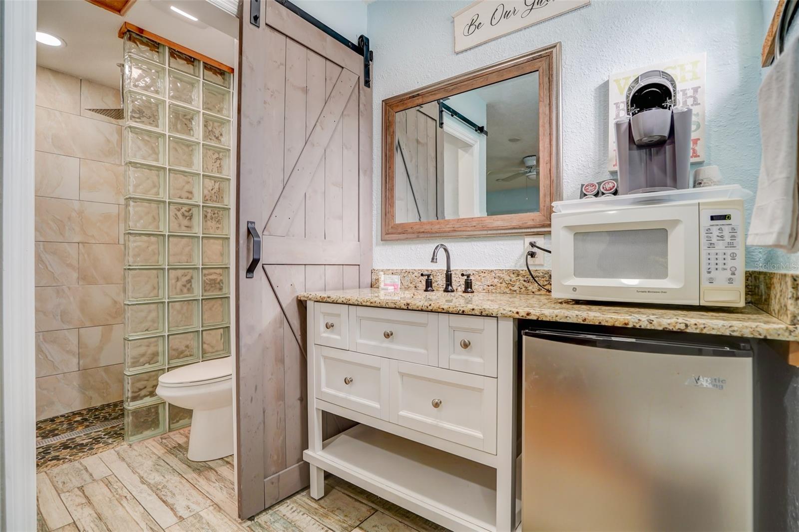 Bathroom vanity with granite counter beside a glass-block shower partition and barn-style sliding door.