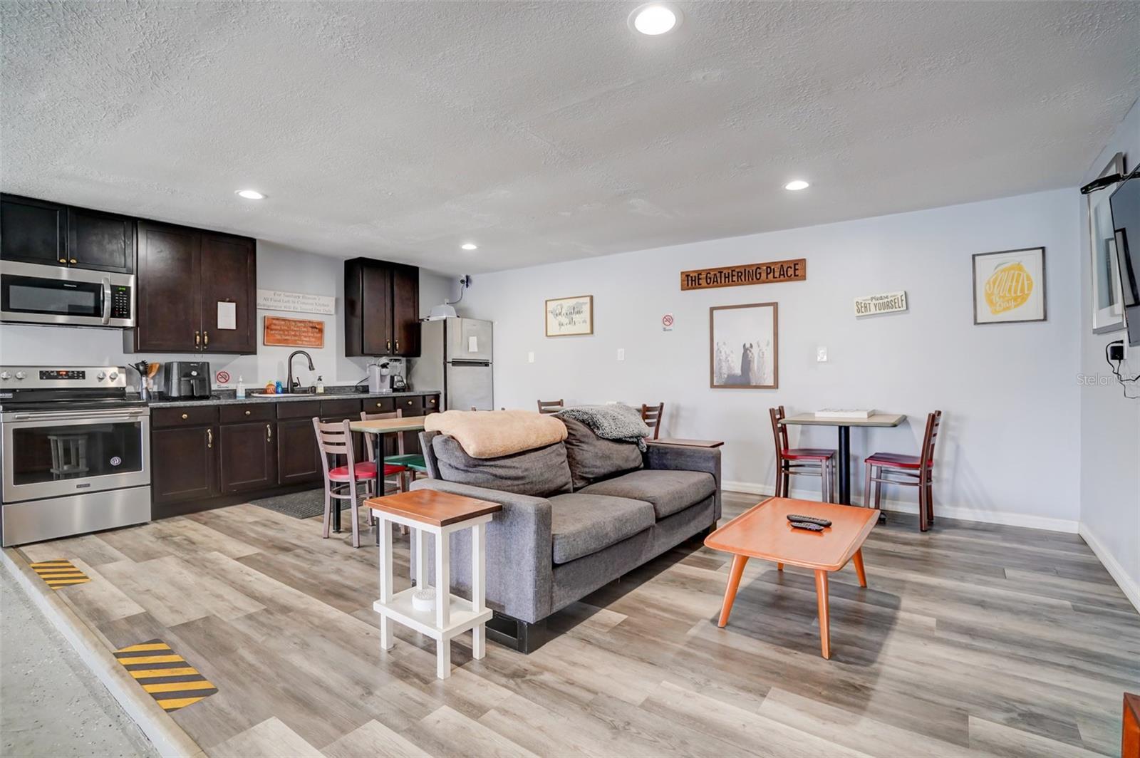 Open-plan kitchen and living area with dark cabinets, a gray sofa, and wood-look flooring.