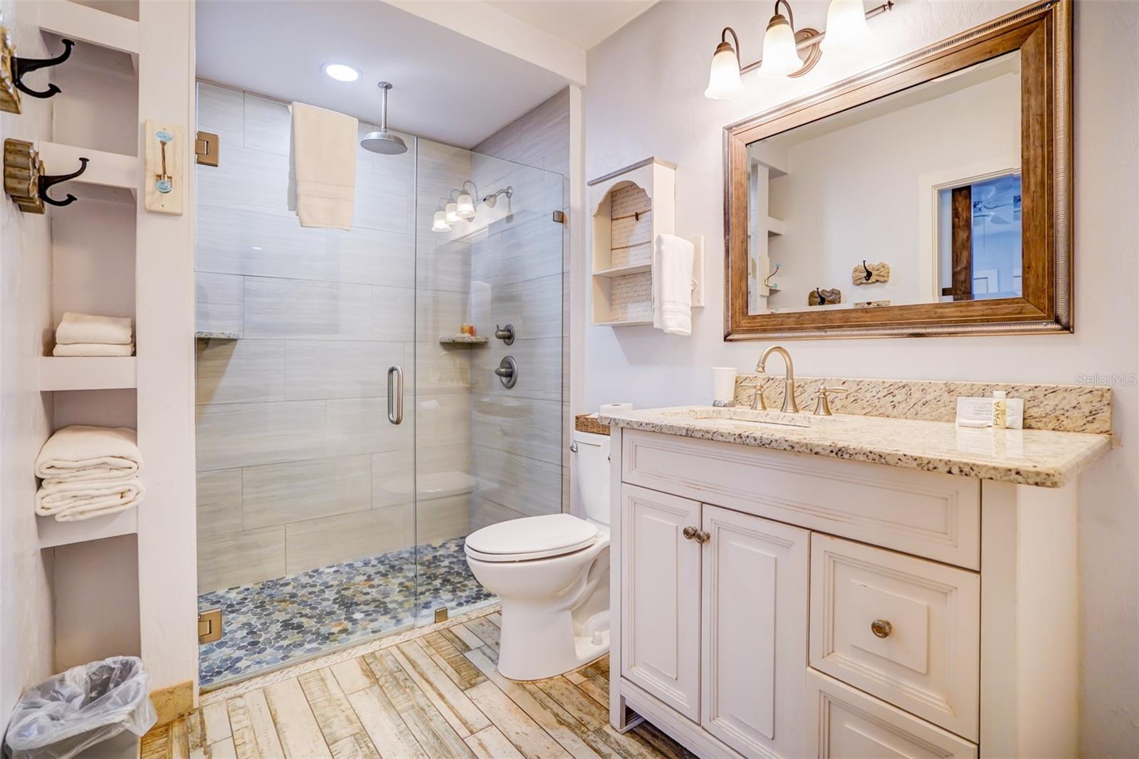 Bathroom with a glass-enclosed shower, pebble floor, and white vanity with granite countertop.