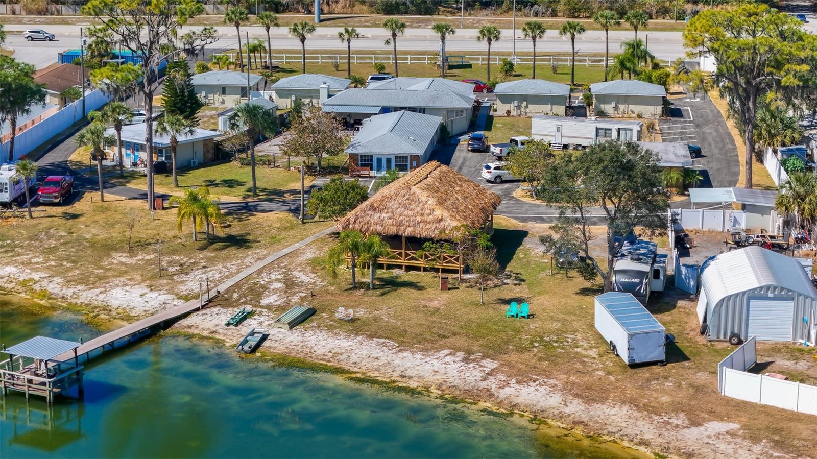 Waterfront property with small buildings, a thatched pavilion, and a dock.