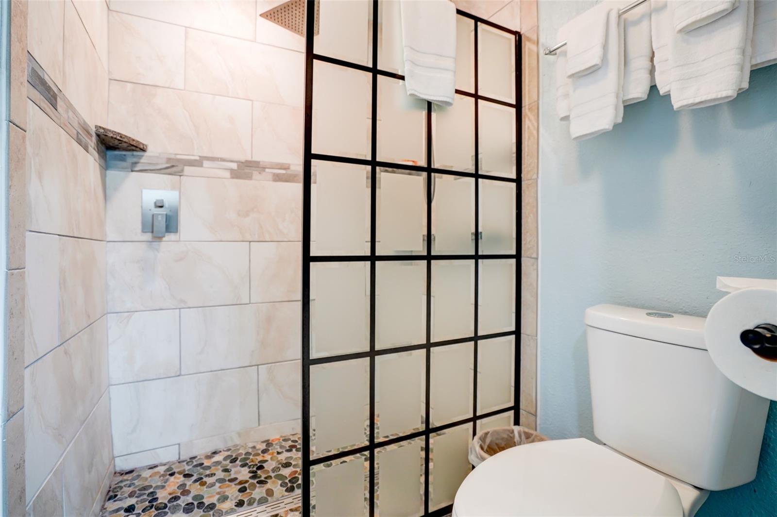 Bathroom with a black grid-frame shower enclosure, marble-look tile, and pebble-stone shower floor.