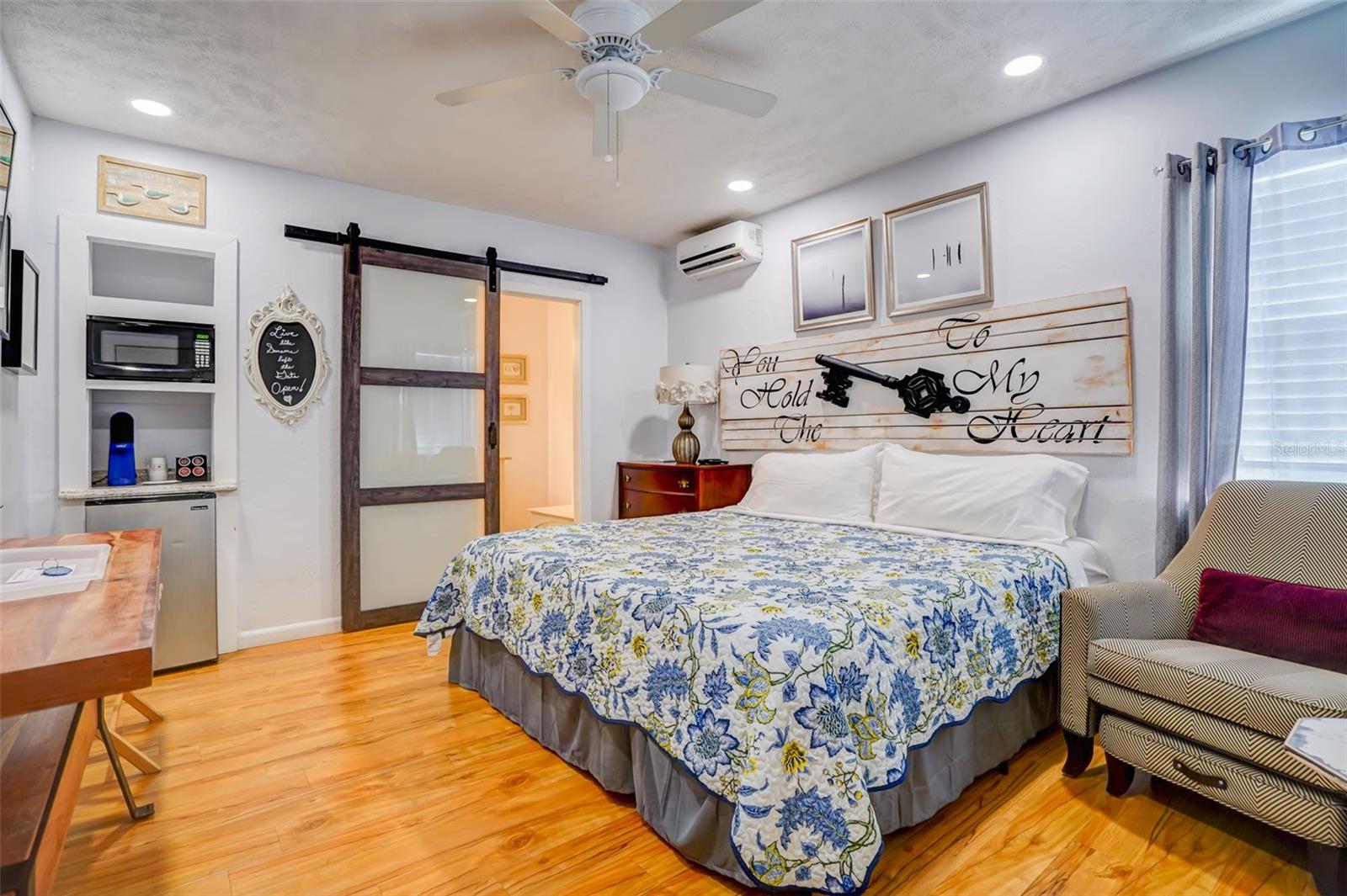 Bedroom with a blue floral bedspread, rustic sliding barn door, and built-in microwave and mini-fridge.