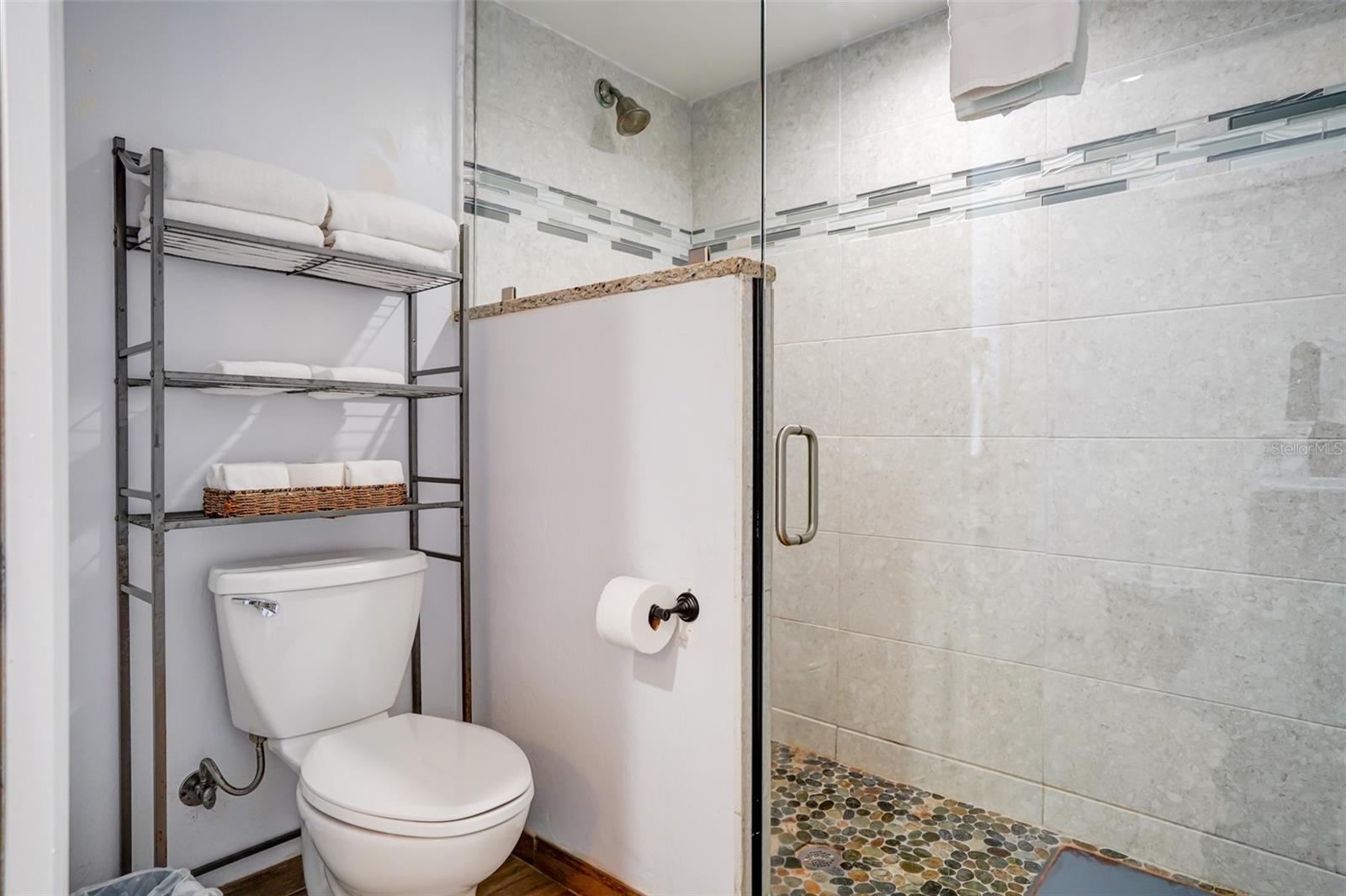 Bathroom with a glass shower, light tiled walls, and pebble shower floor.