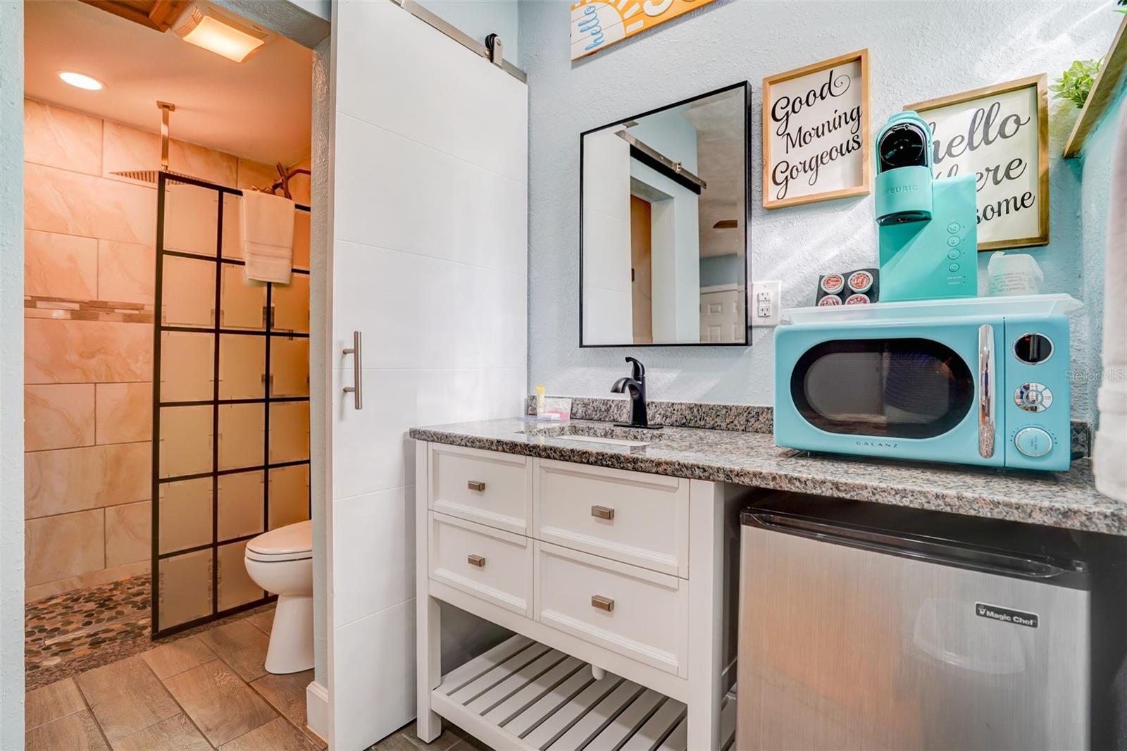 Bathroom vanity with granite counter beside a black-framed, glass-enclosed shower.
