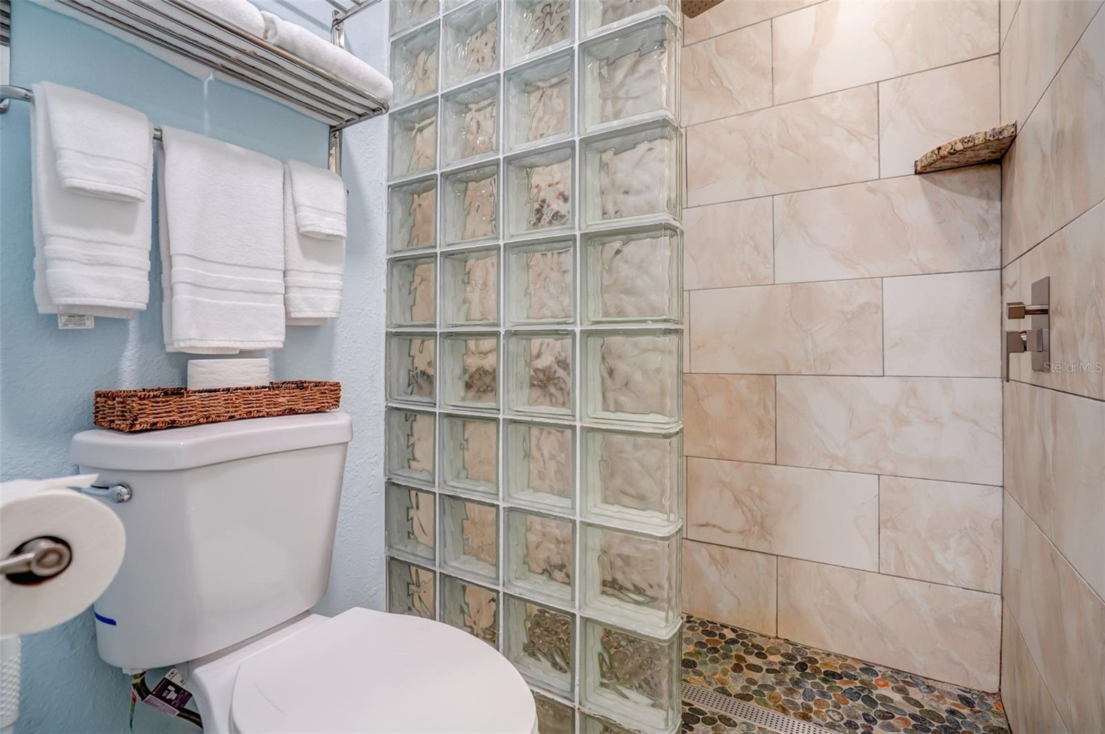 Bathroom with a glass-block shower partition, beige tile walls, and a pebble shower floor.